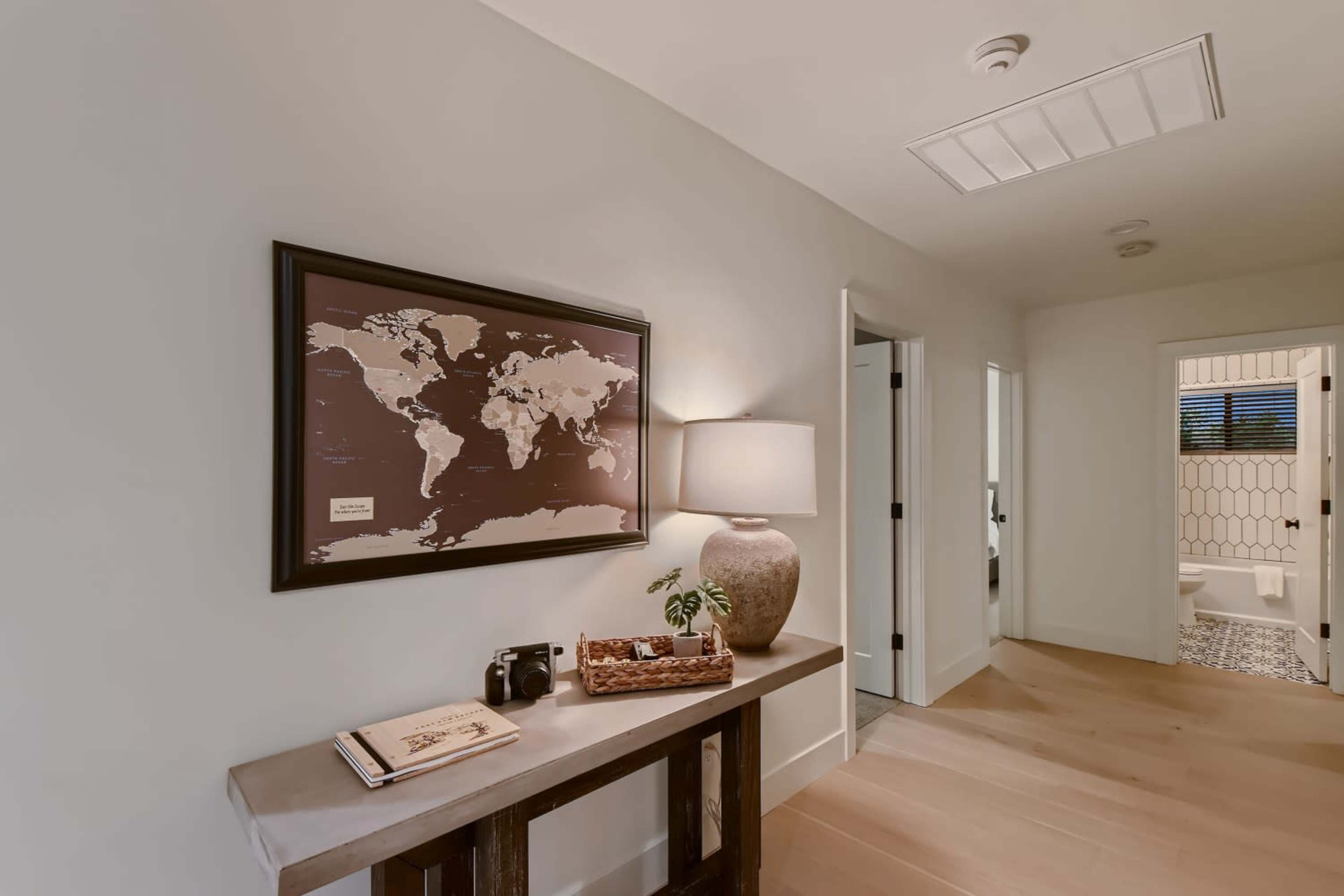 A hallway featuring a world map on the wall, a lamp on a side table, and a doorway leading to a bathroom.