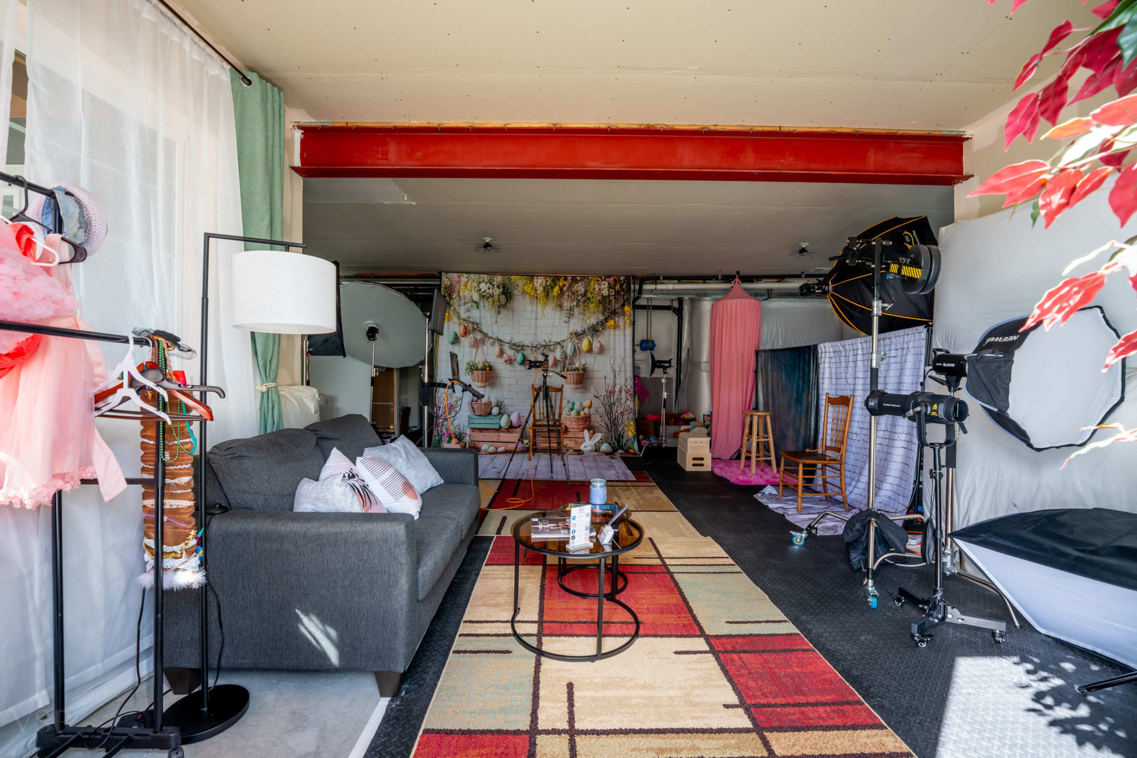 The image shows a studio space set up for photography, featuring a sofa, backdrop decorations, lighting equipment, and chairs.