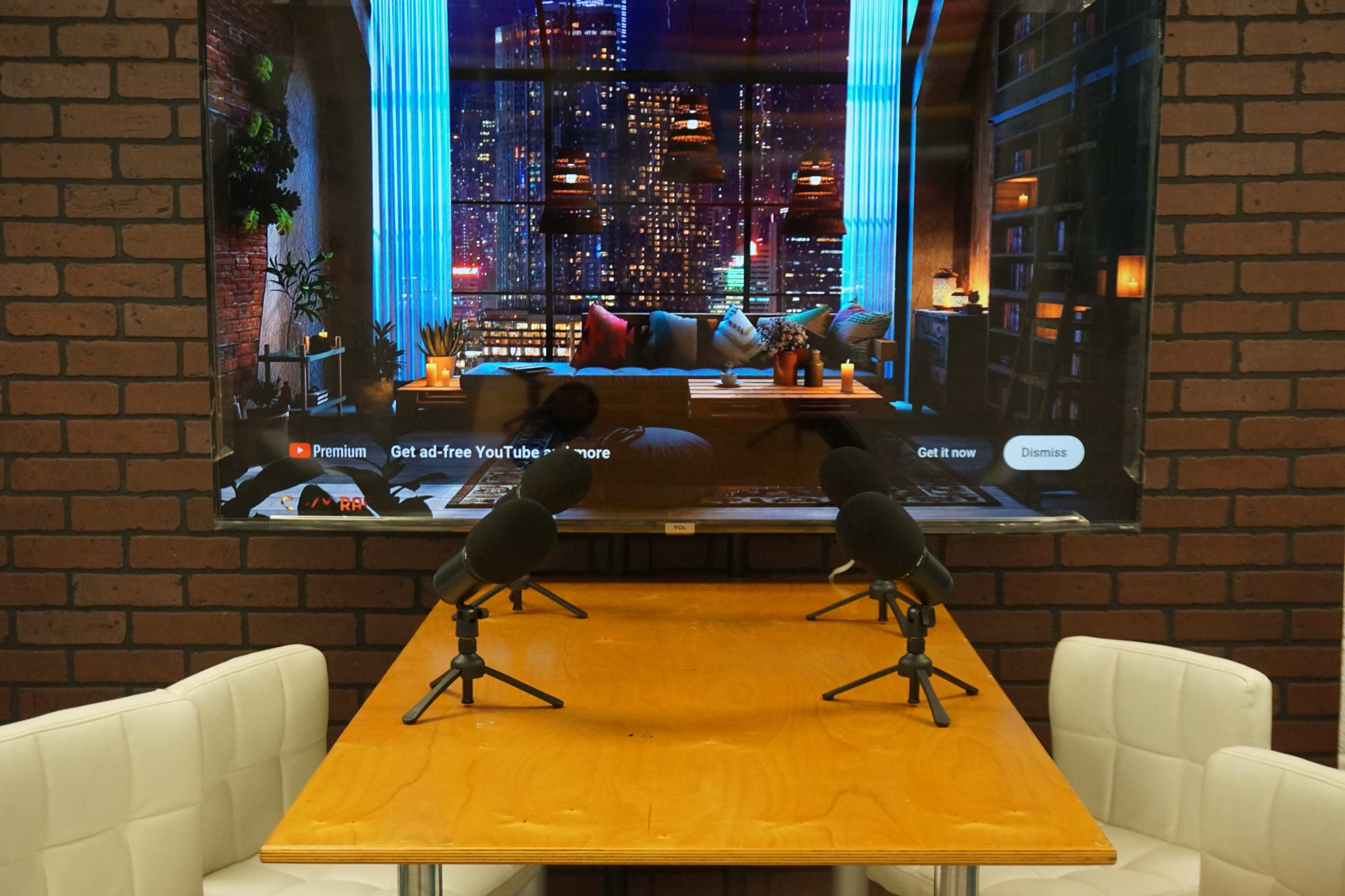 A wooden table with two microphones sits in front of a large screen displaying a city skyline at night.