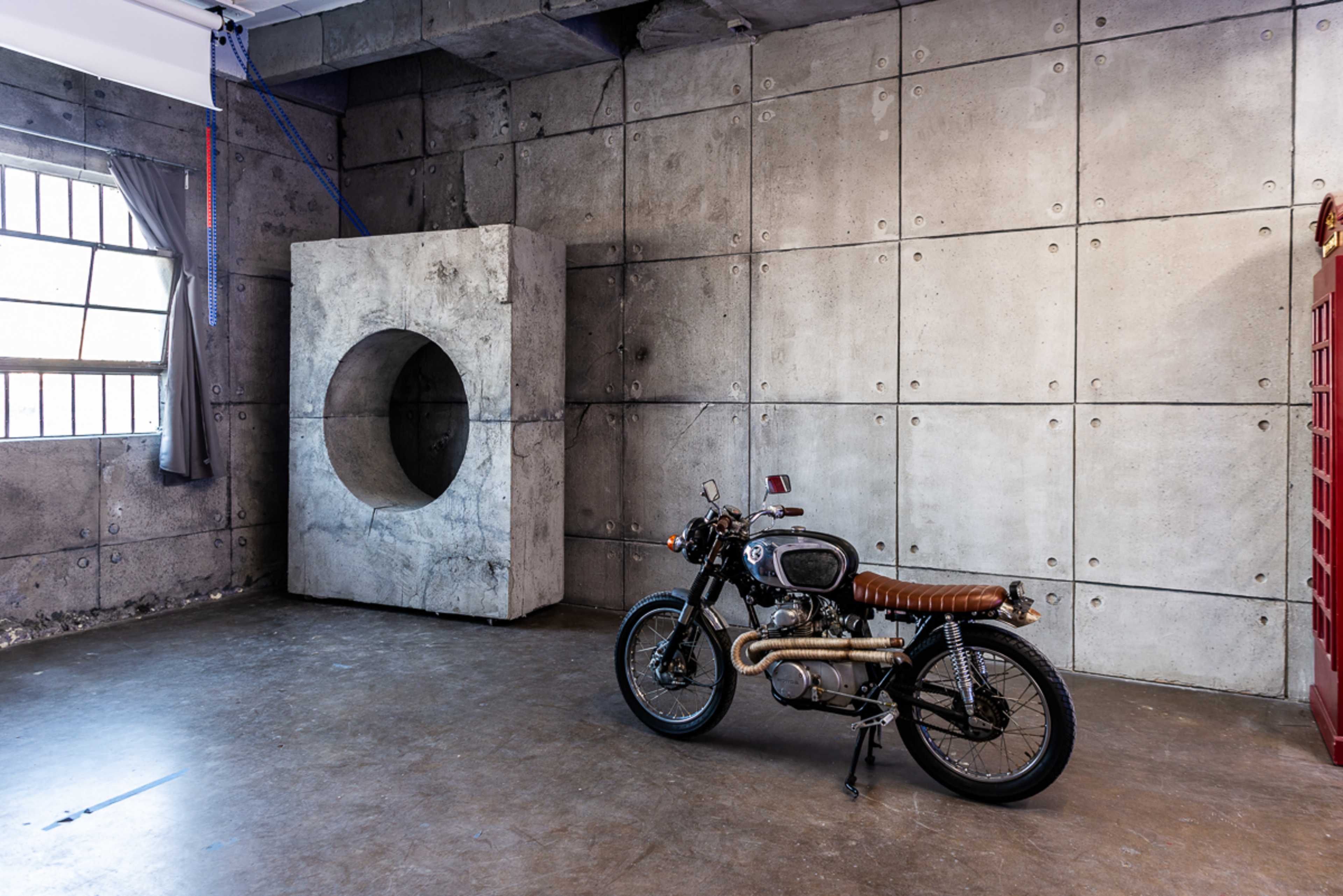 A motorcycle is positioned next to a large concrete structure with a circular opening in an industrial-style room.