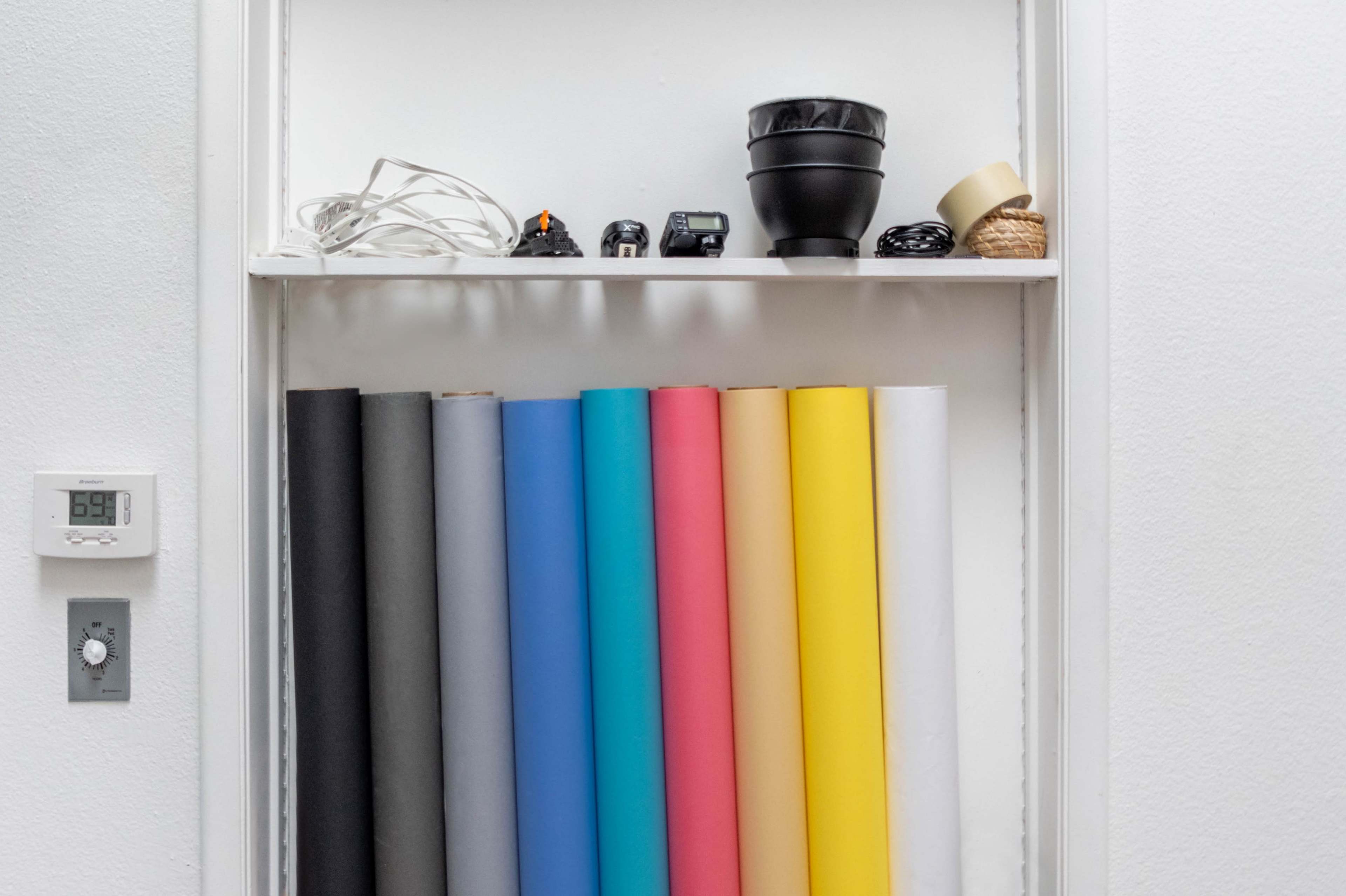A shelf containing various items, including colorful rolls of paper, a small pot, cameras, and a bundle of cords.