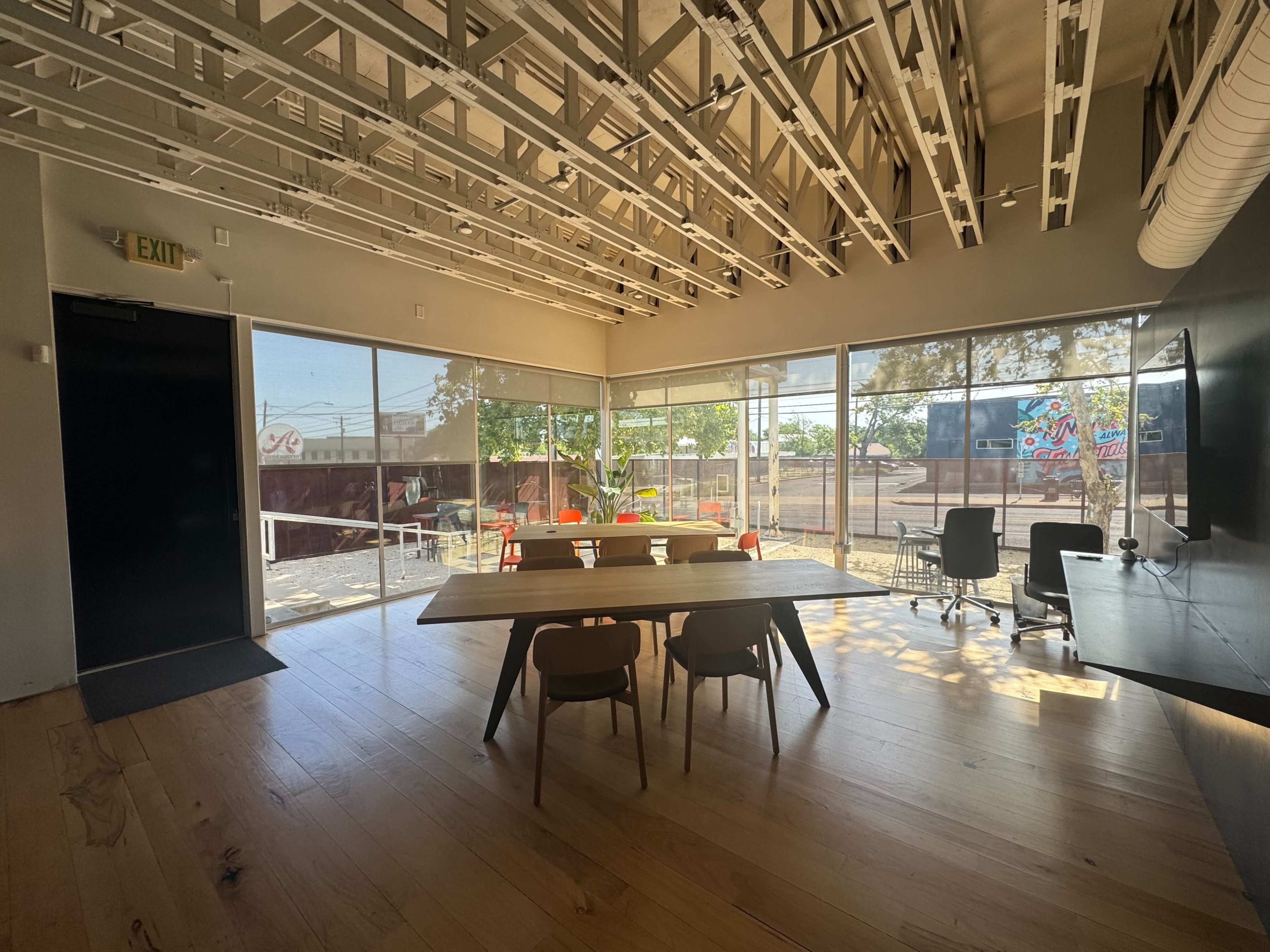 A spacious conference room features a large wooden table, modern chairs, and large windows that offer views of an outdoor area.