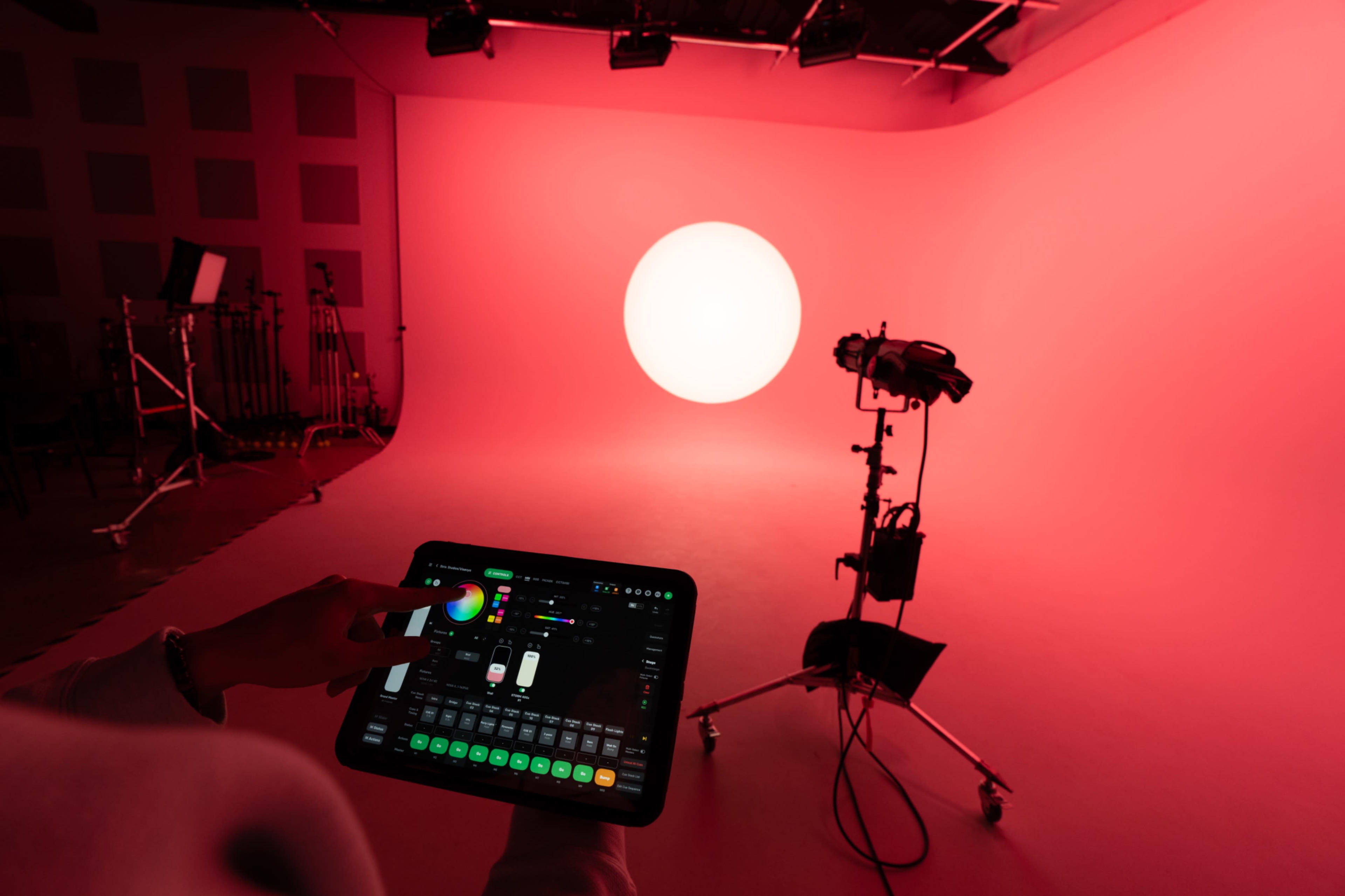 A person is using a tablet to adjust lighting in a photography studio with a large lit circular backdrop.