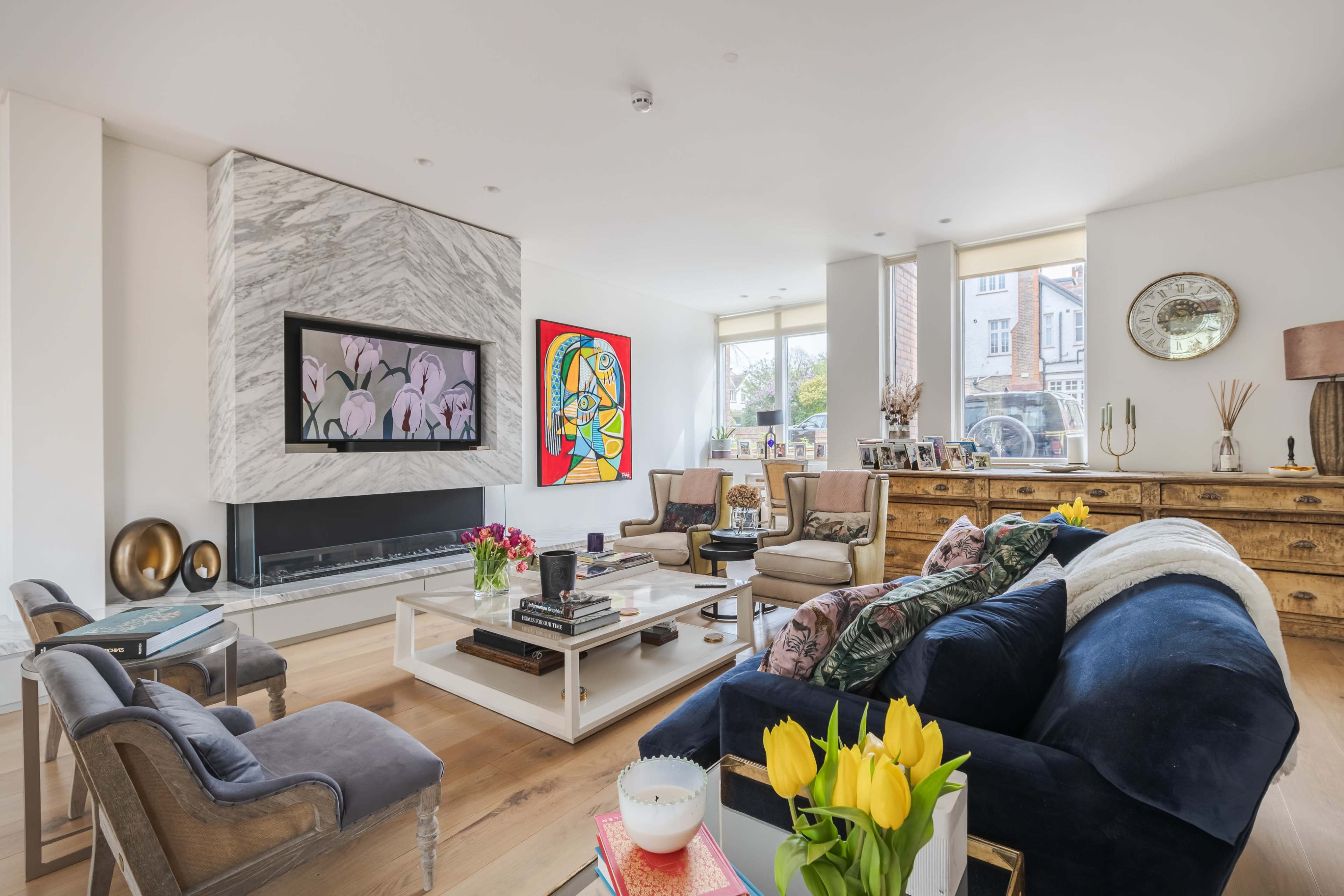 The living room features a marble fireplace, large windows, colorful artwork, and a mix of modern and traditional furnishings.