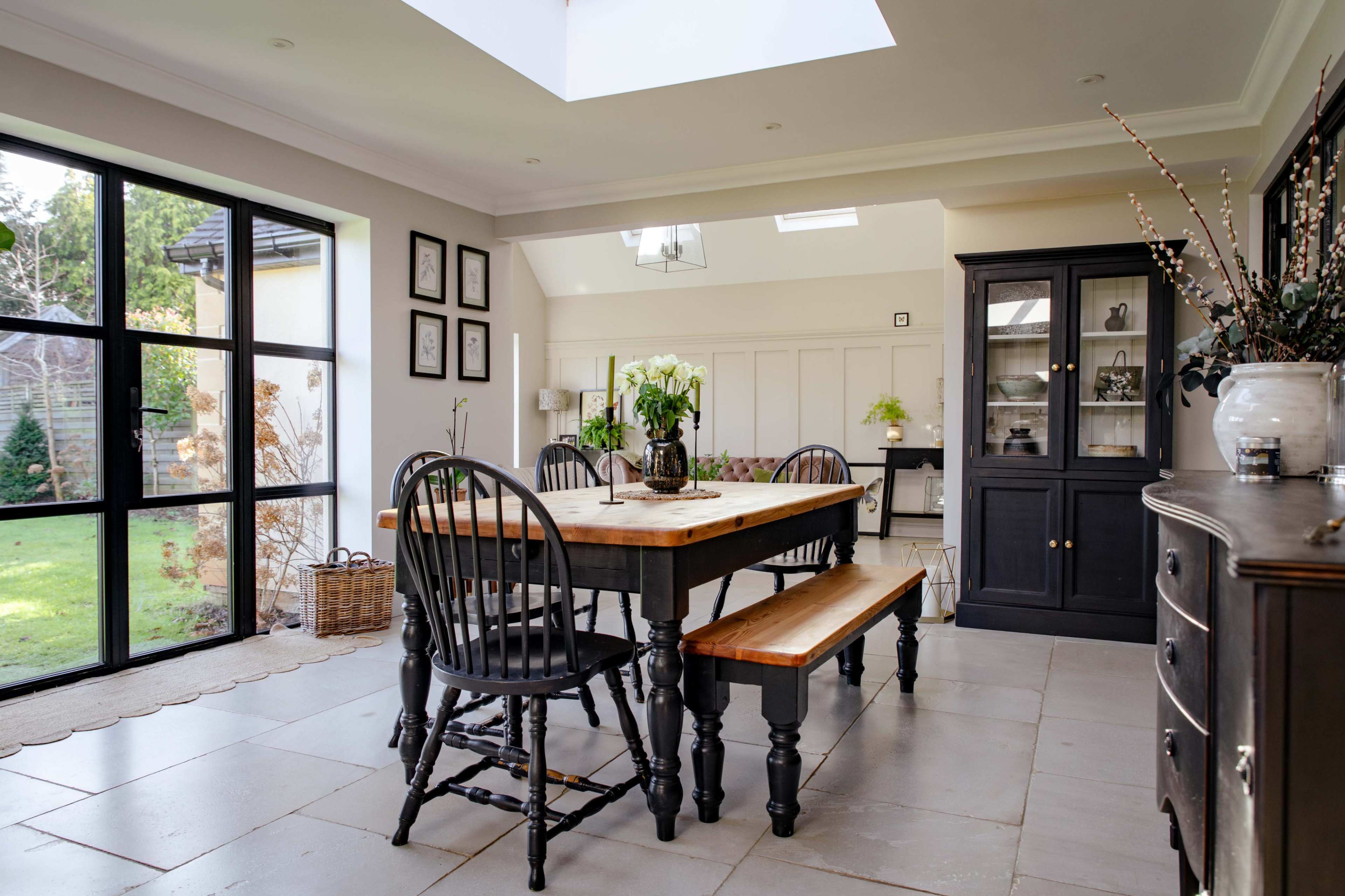 The image features a modern dining area with a wooden table and benches, surrounded by large windows allowing natural light to fill the space.