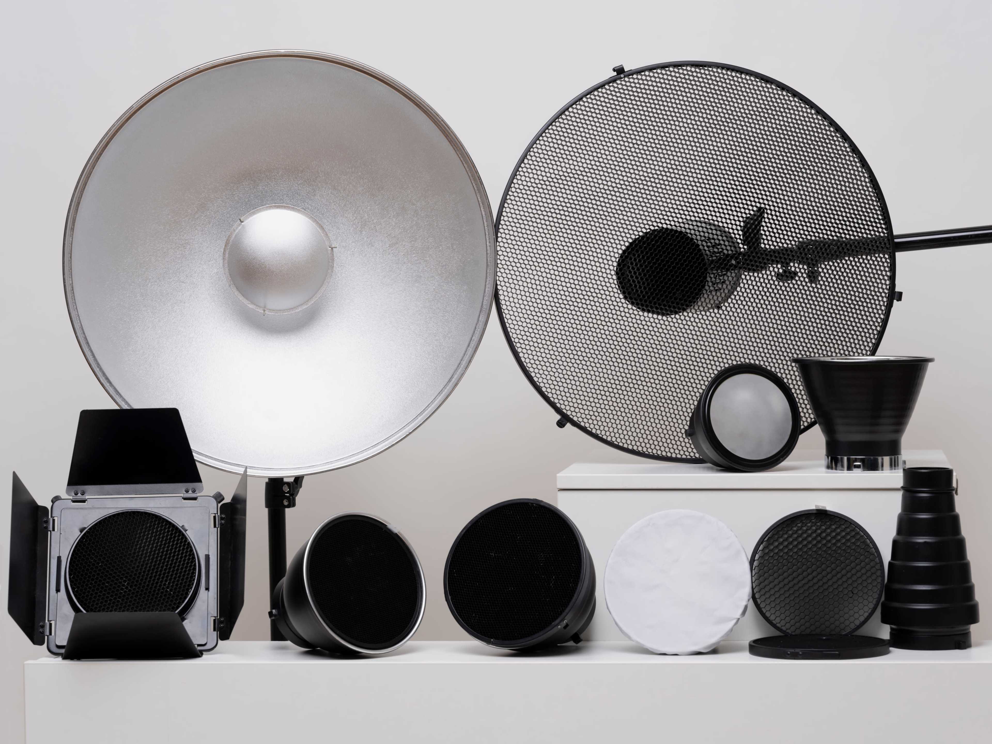 The image displays a variety of photography light modifiers, including reflectors and diffusers, arranged on a white background.