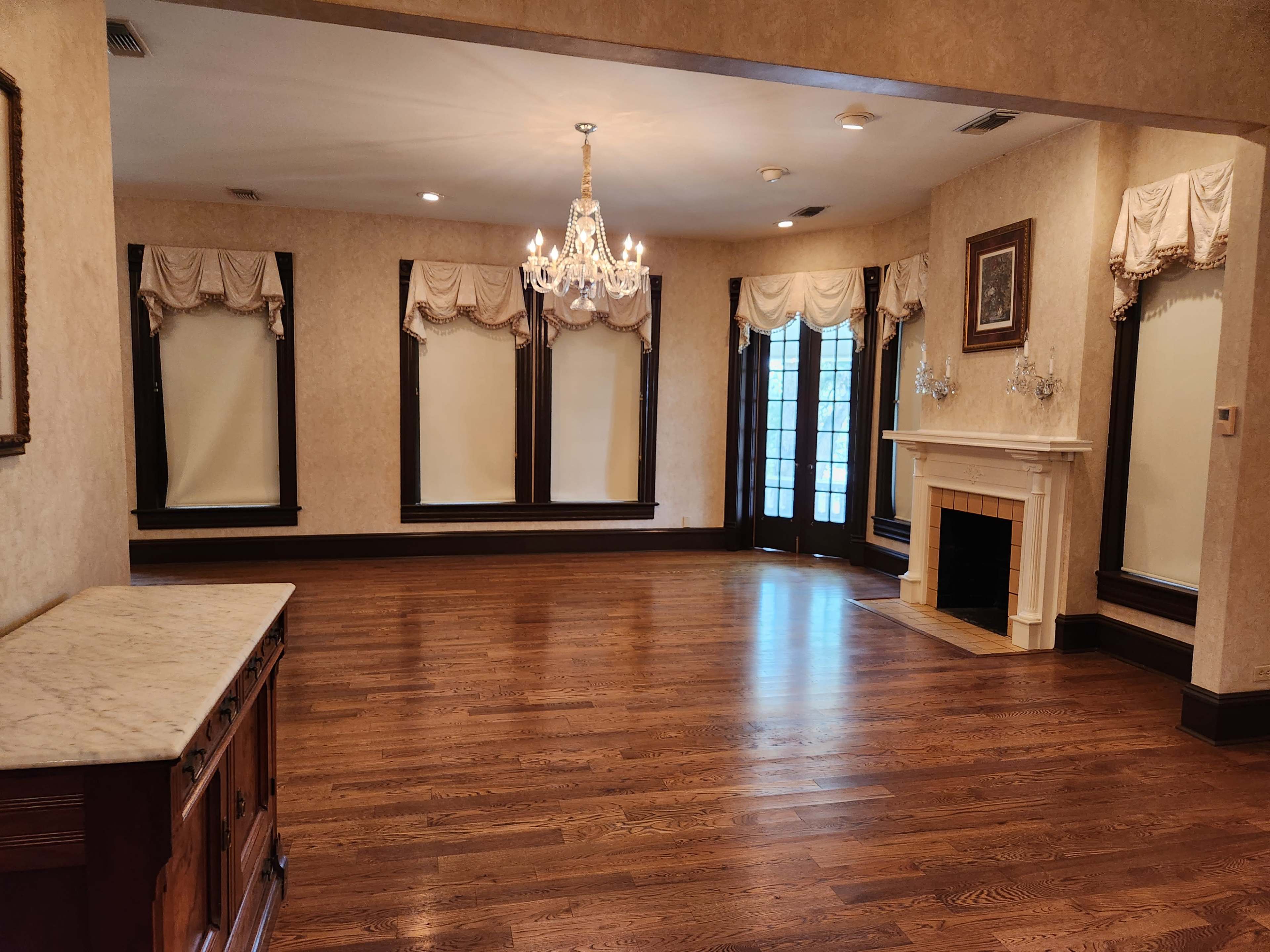The room features hardwood flooring, a fireplace, and large windows dressed with elegant drapes.