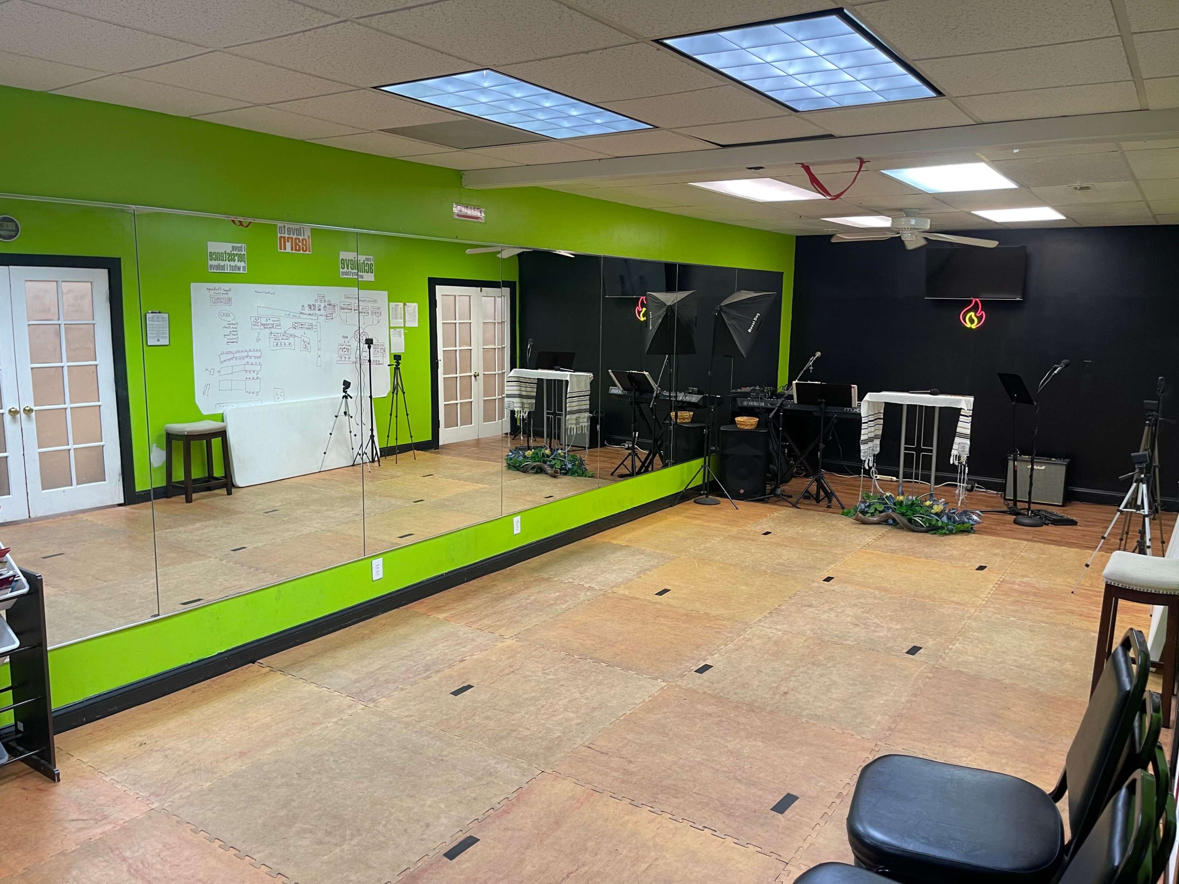 A well-lit studio space with a mirrored wall, black and green walls, musical equipment, and cameras set up for recording or practice.
