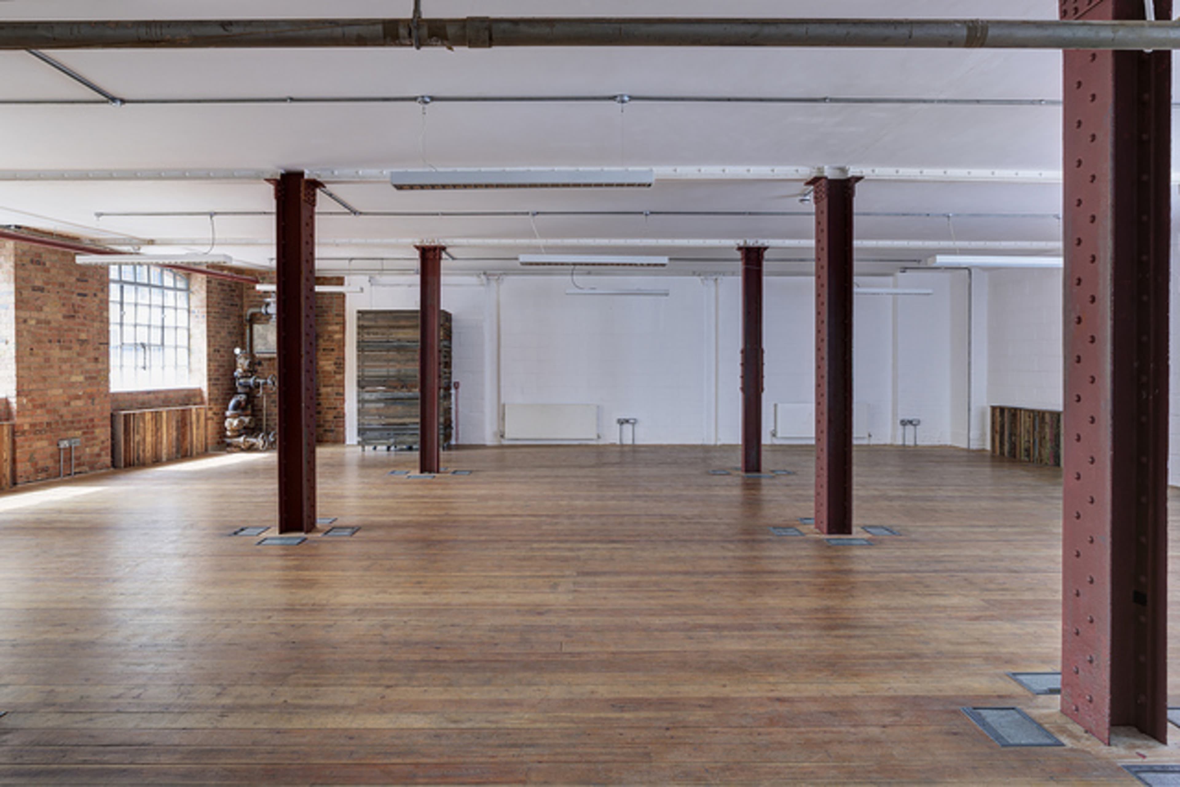 An empty, industrial-style room with wooden floors and exposed metal columns.