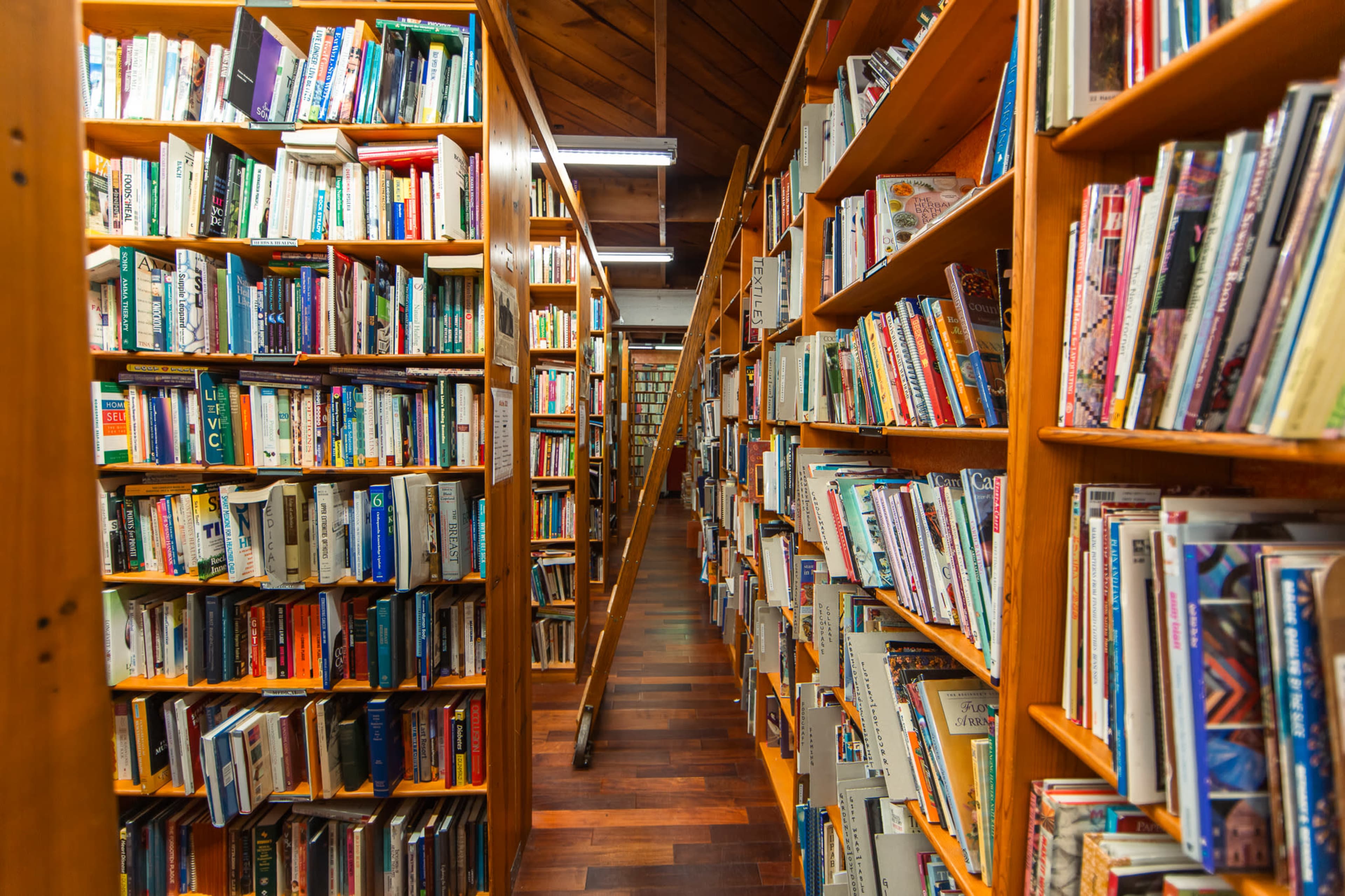 The image shows a narrow aisle lined with wooden bookshelves filled with various books on either side.