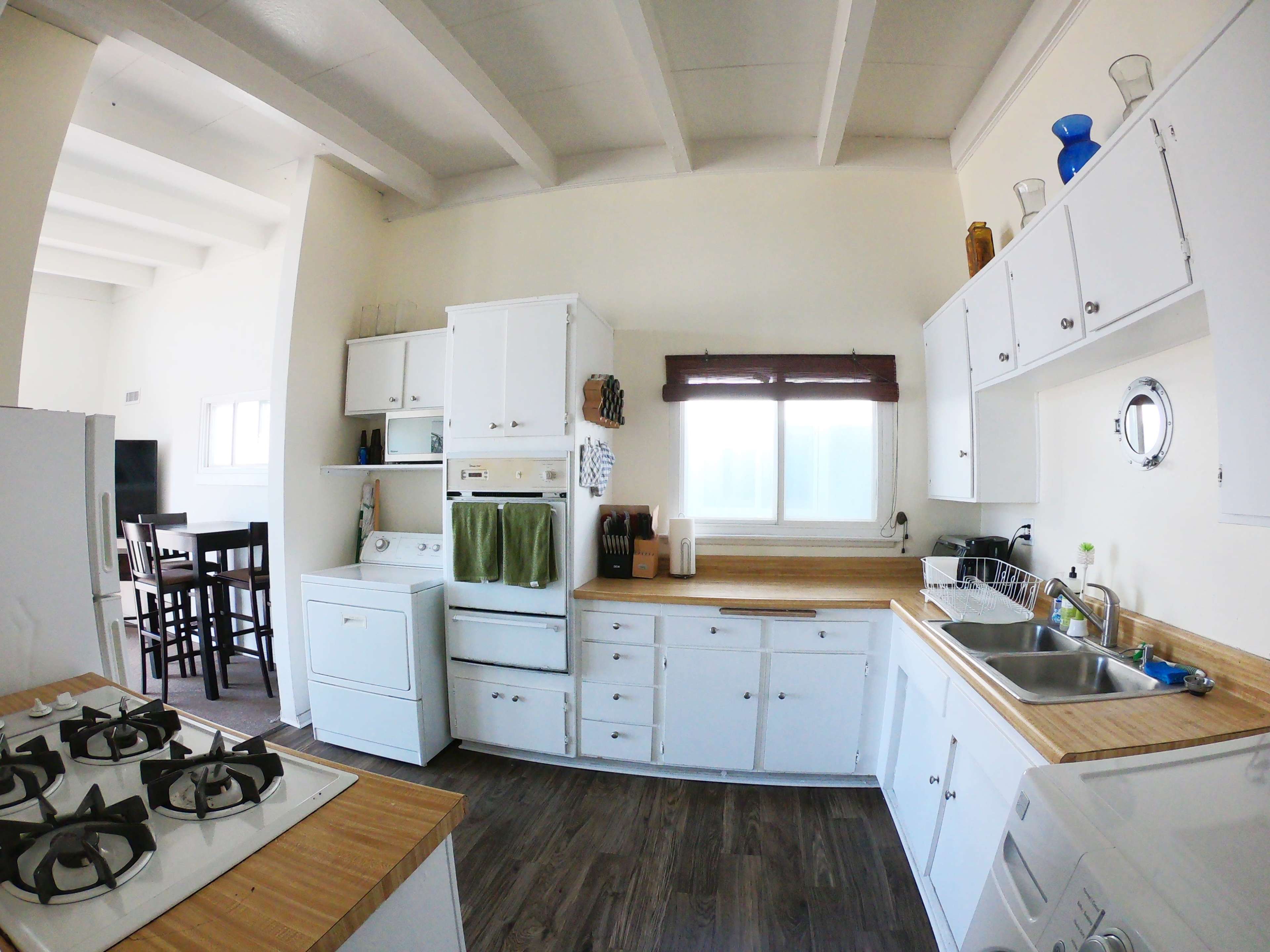A bright, airy kitchen with white cabinets, a wooden countertop, and a stove, featuring a window above the sink.