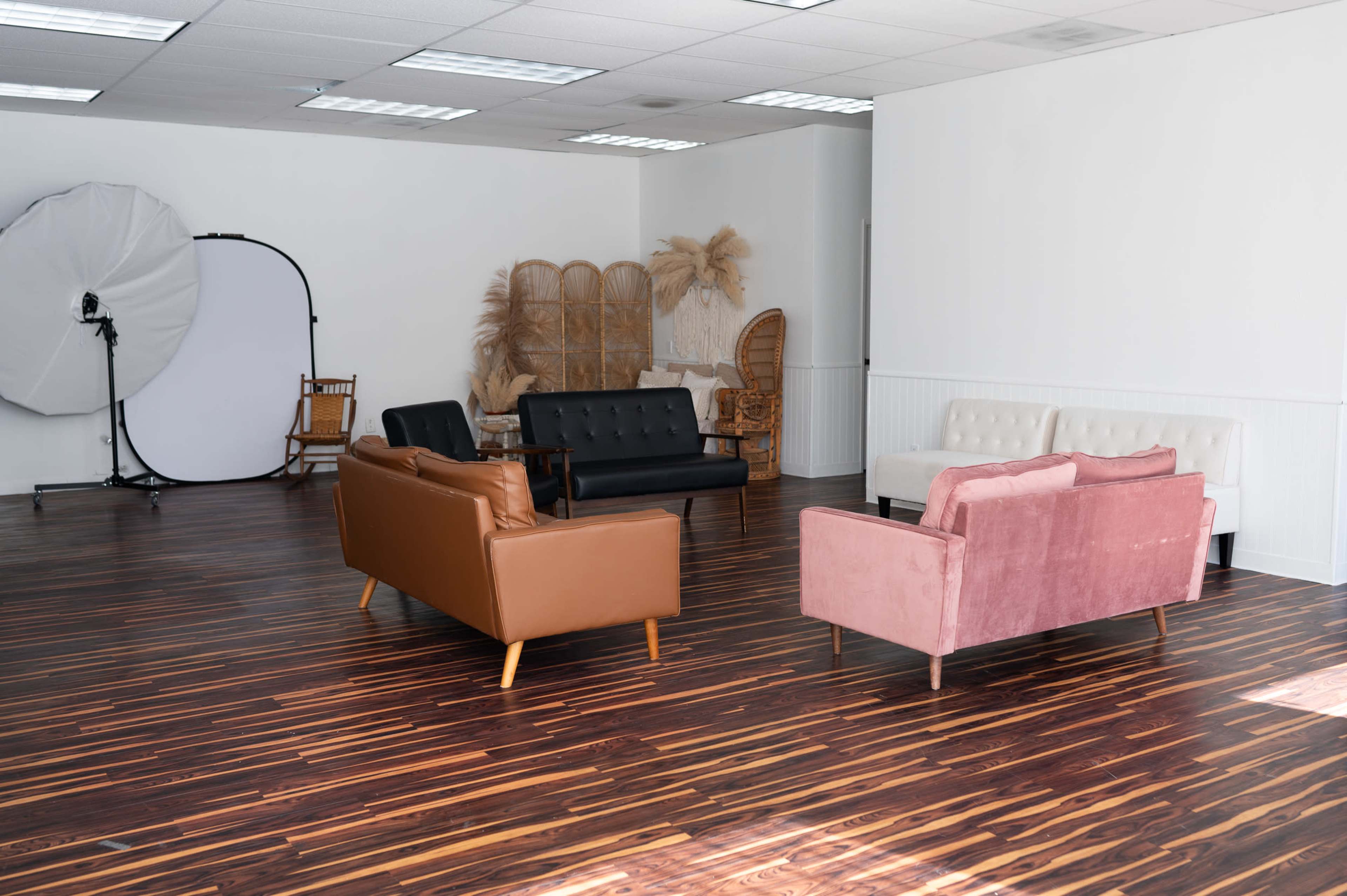 The image shows a spacious room with hardwood floors featuring several couches arranged in a seating area, along with a photography backdrop and decorative elements in the background.