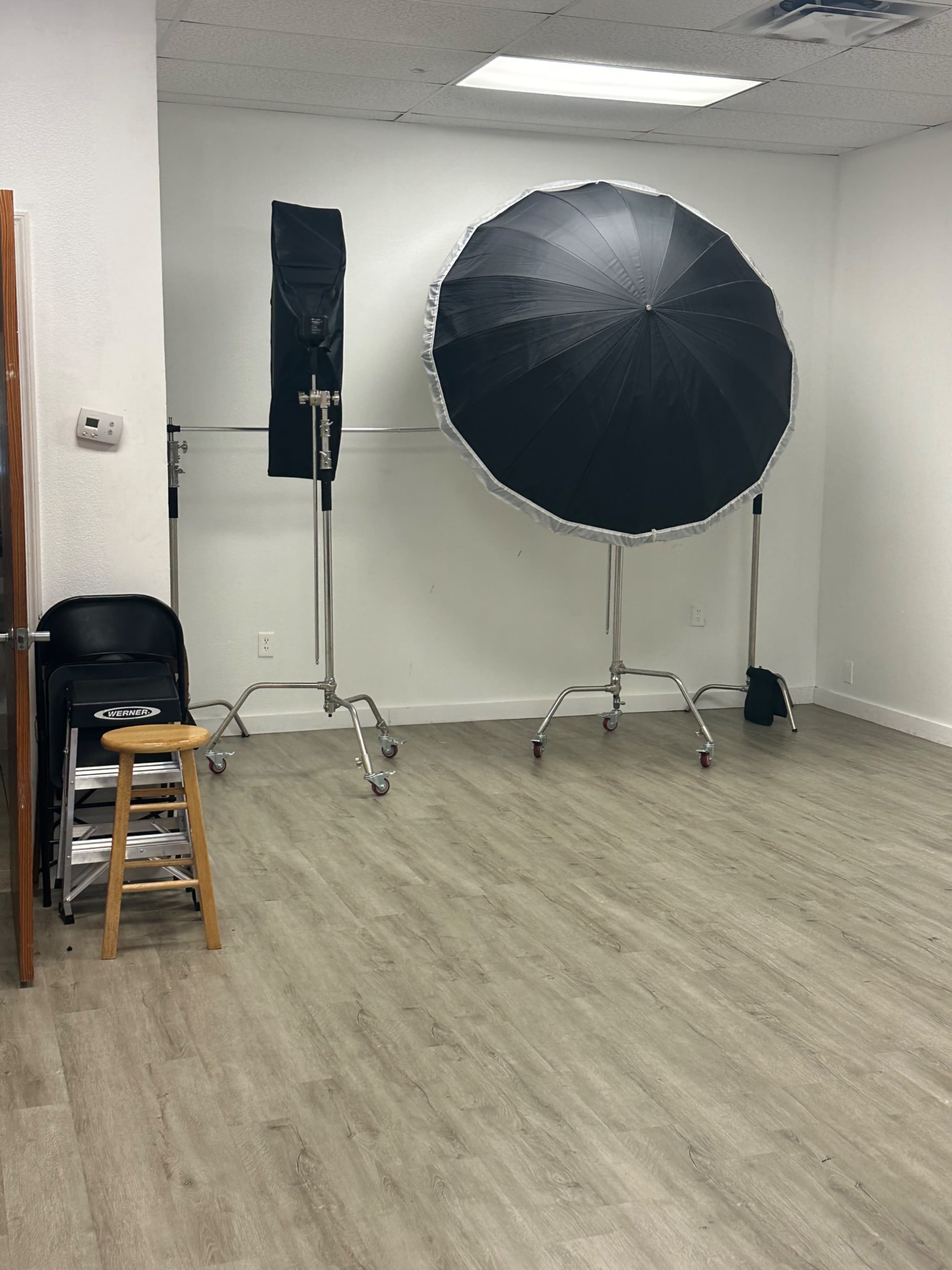 A sparse room with two large lighting umbrellas on stands and a chair next to a wooden stool.