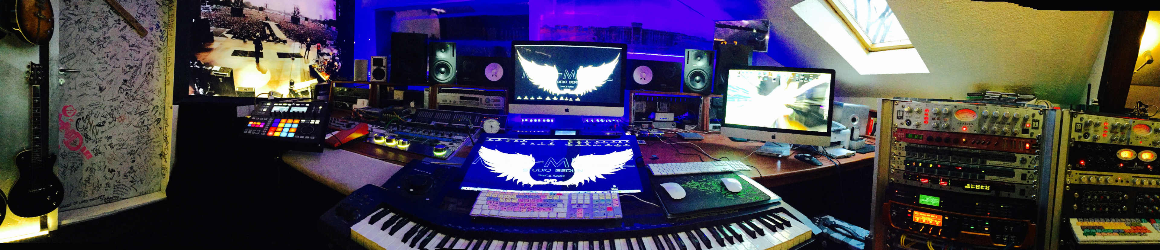 A music production studio filled with various electronic equipment, computers, and monitors displaying visual graphics in a vibrant setting.