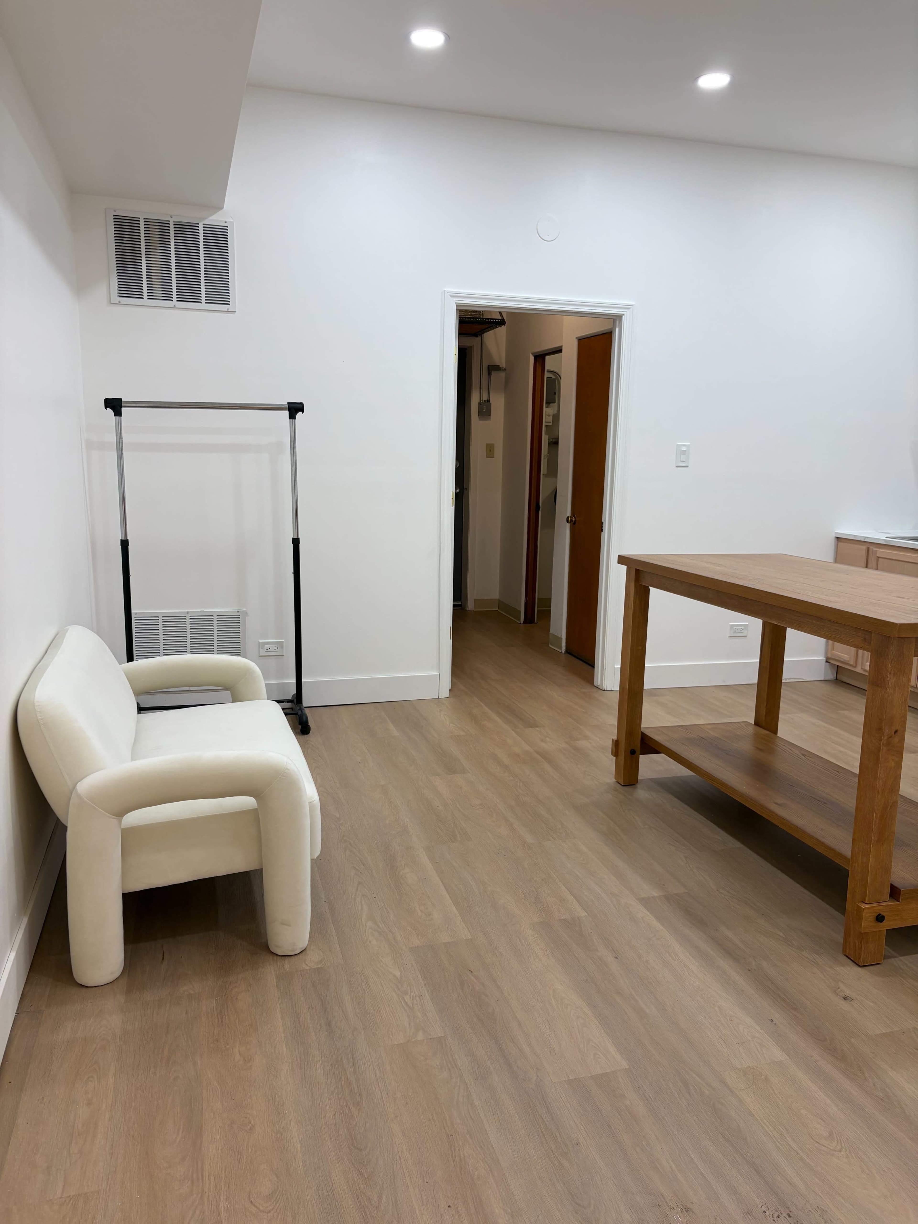 The image shows a minimalistic room with a white couch, a wooden table, and a door leading to another space.