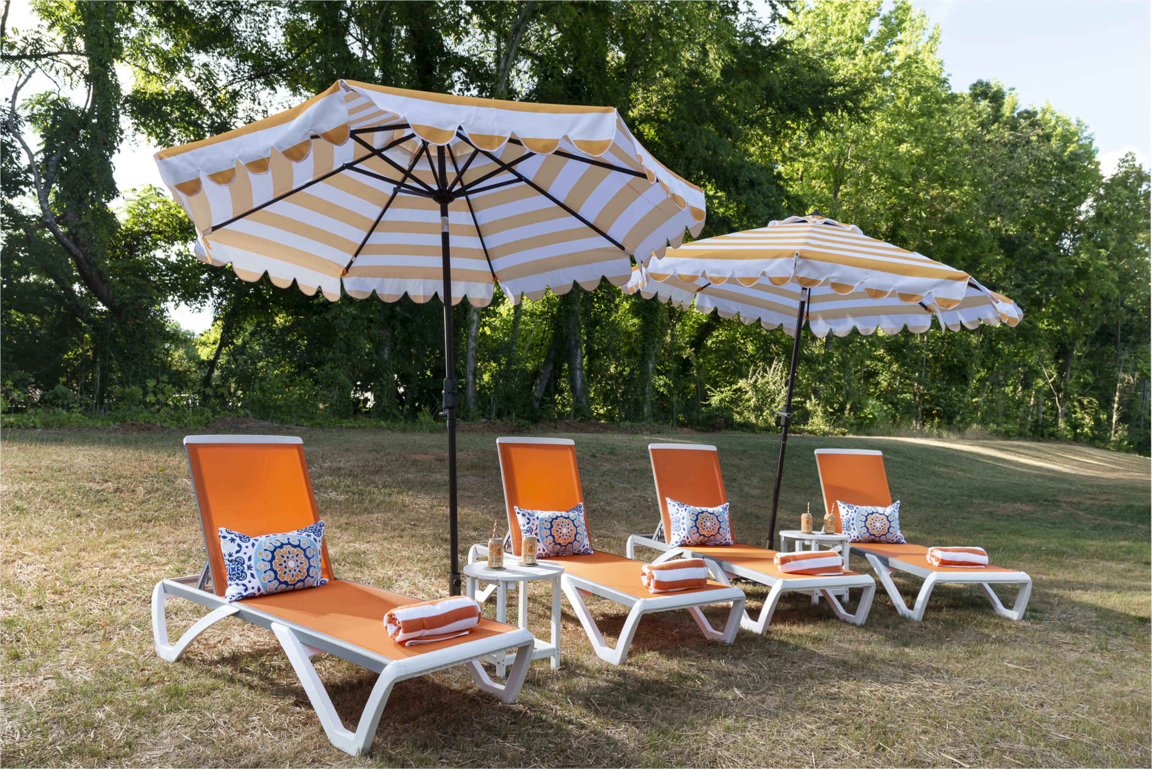 Four orange and white striped lounge chairs with matching umbrellas are arranged on a grassy area under trees.