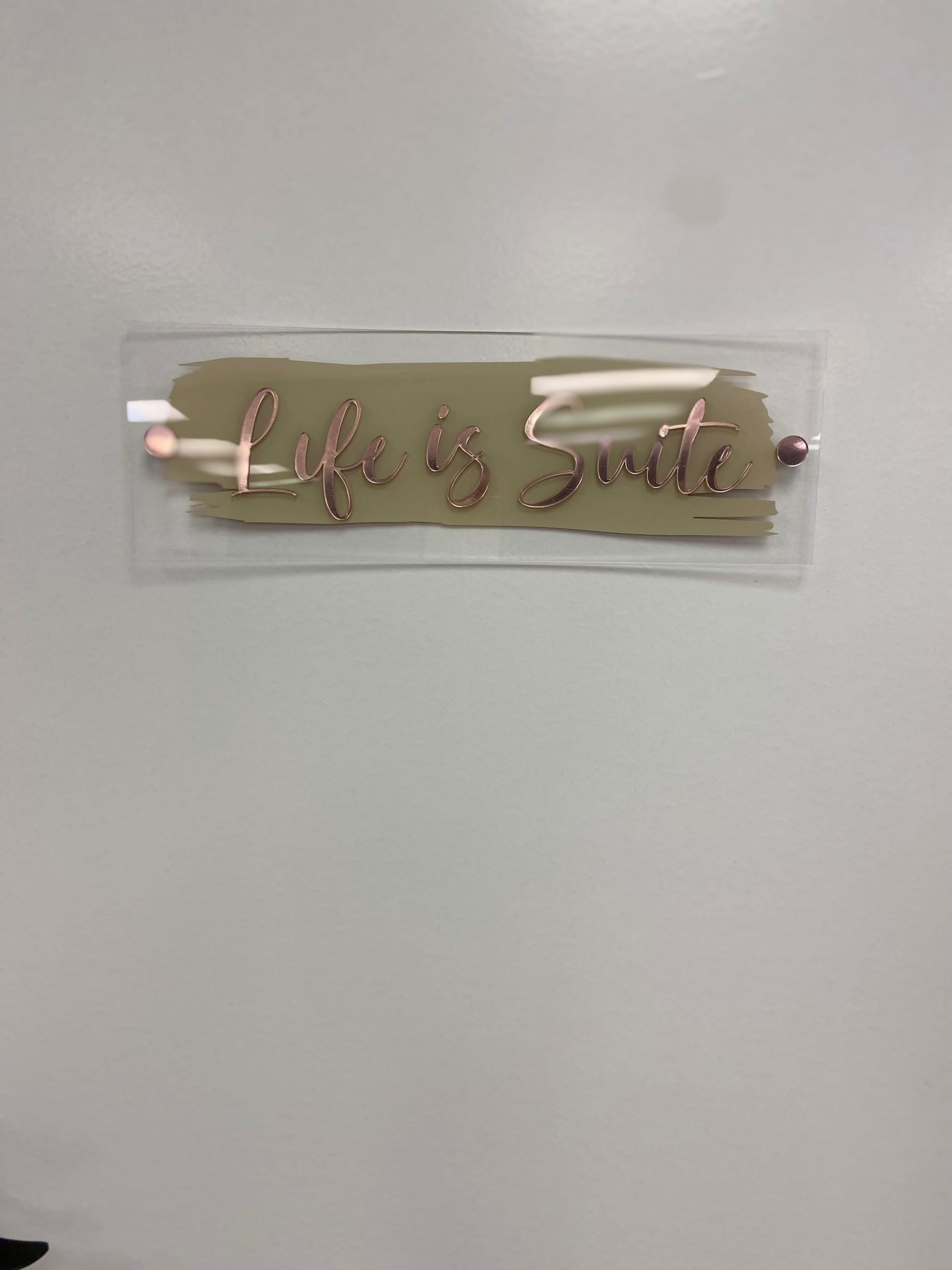 A transparent sign displaying the phrase "Life is Suite" is mounted on a plain wall.