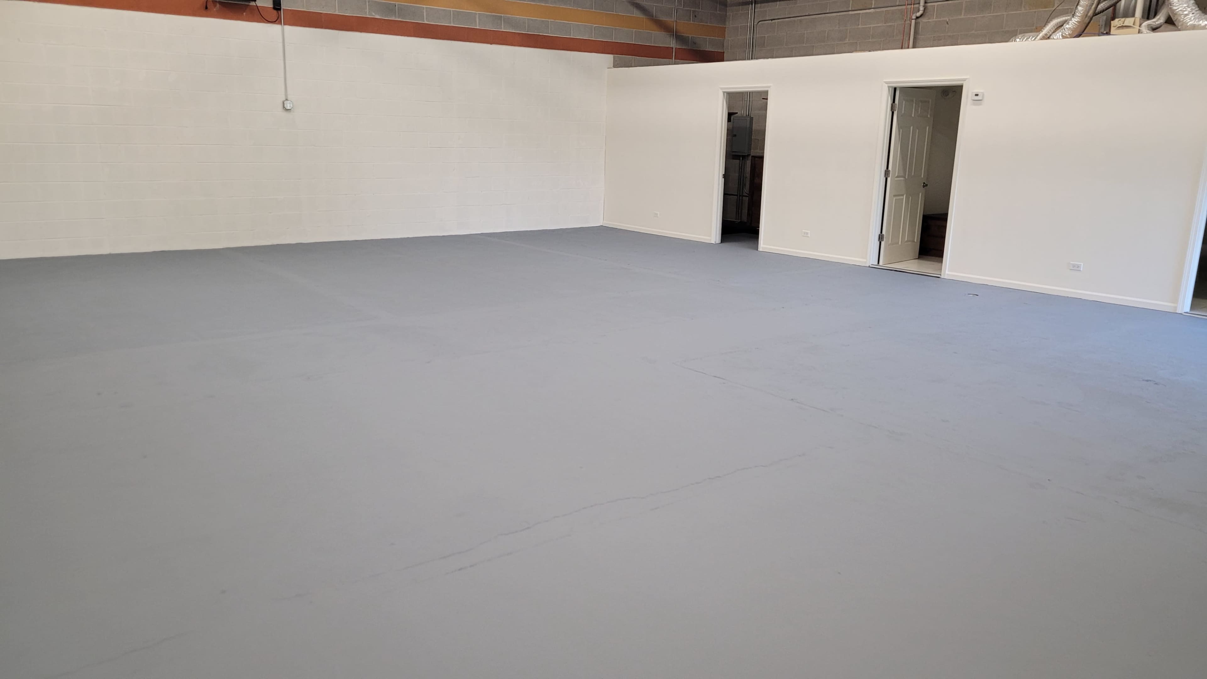 A spacious, empty room with a gray floor and two doorways leading to other areas.