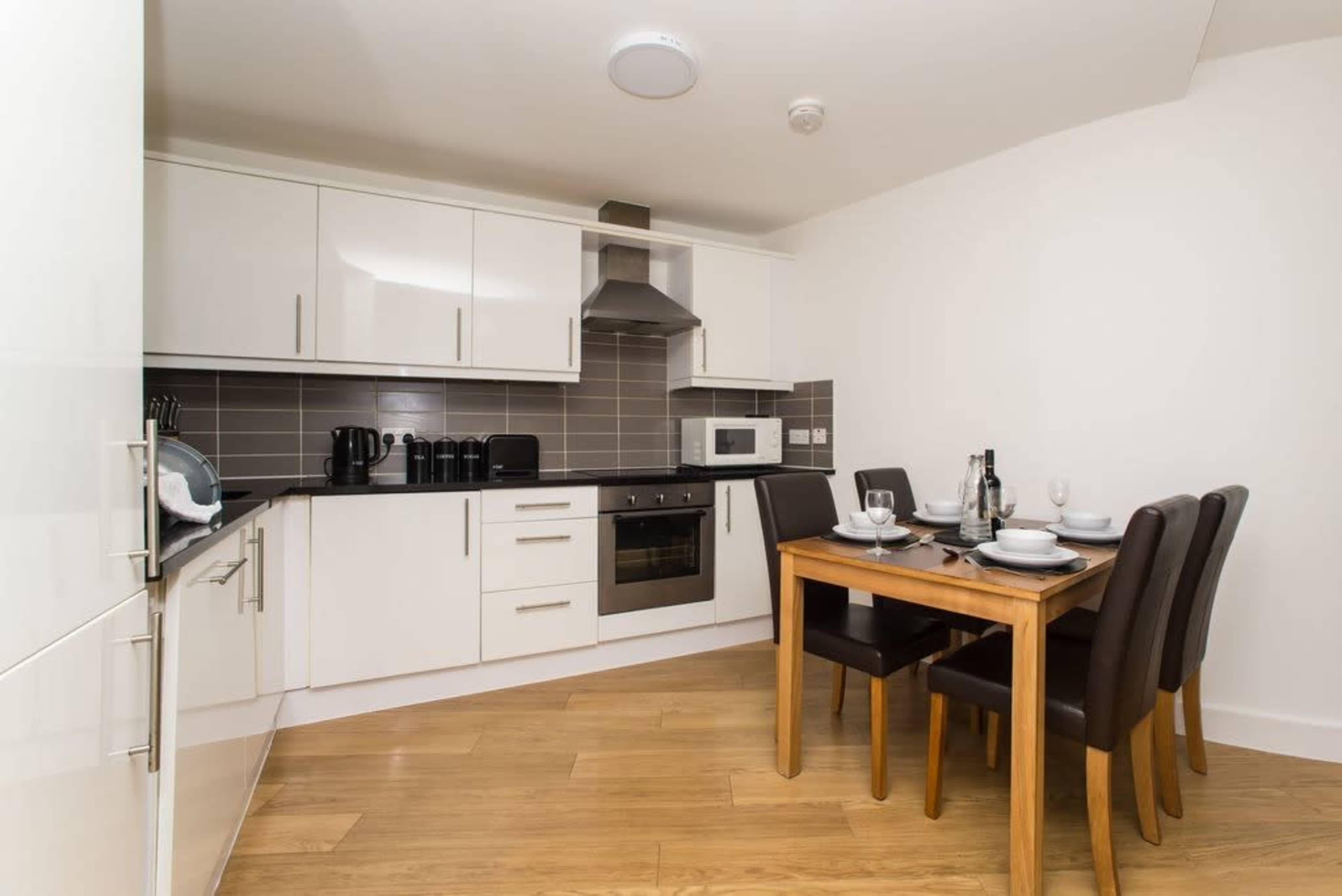 A modern kitchen features white cabinets, a dark countertop, and a small dining table set for four.