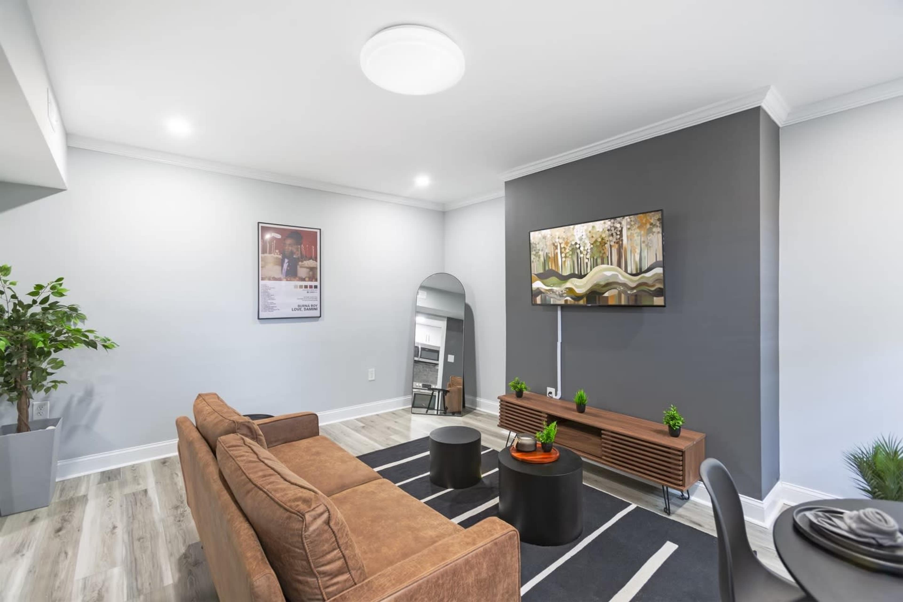 A modern living room featuring a brown couch, a round black coffee table, a large wall-mounted painting, and a potted plant in the corner.