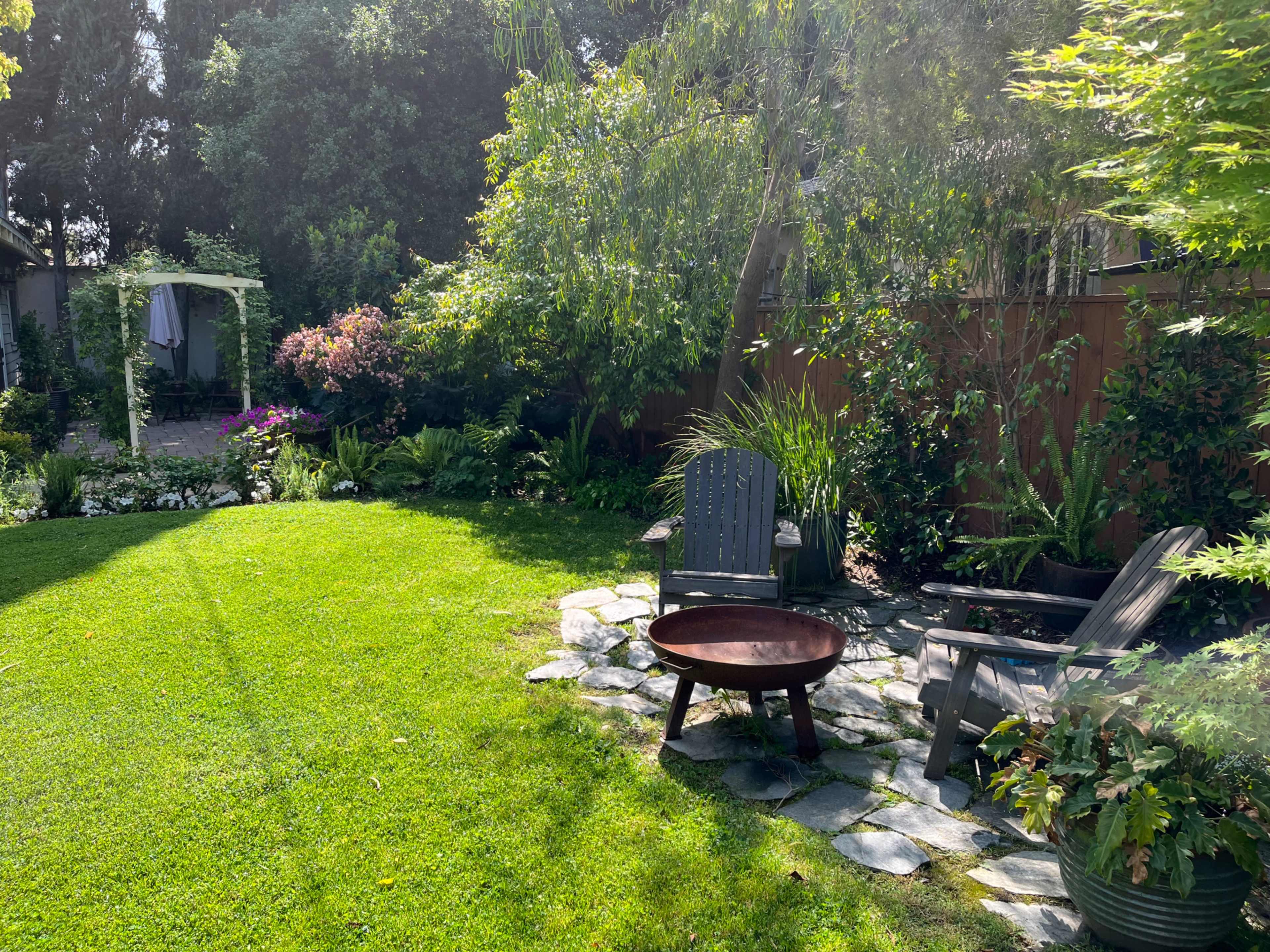 A well-maintained garden with a grassy area, stone pathway, and seating arrangement beside a fire pit.