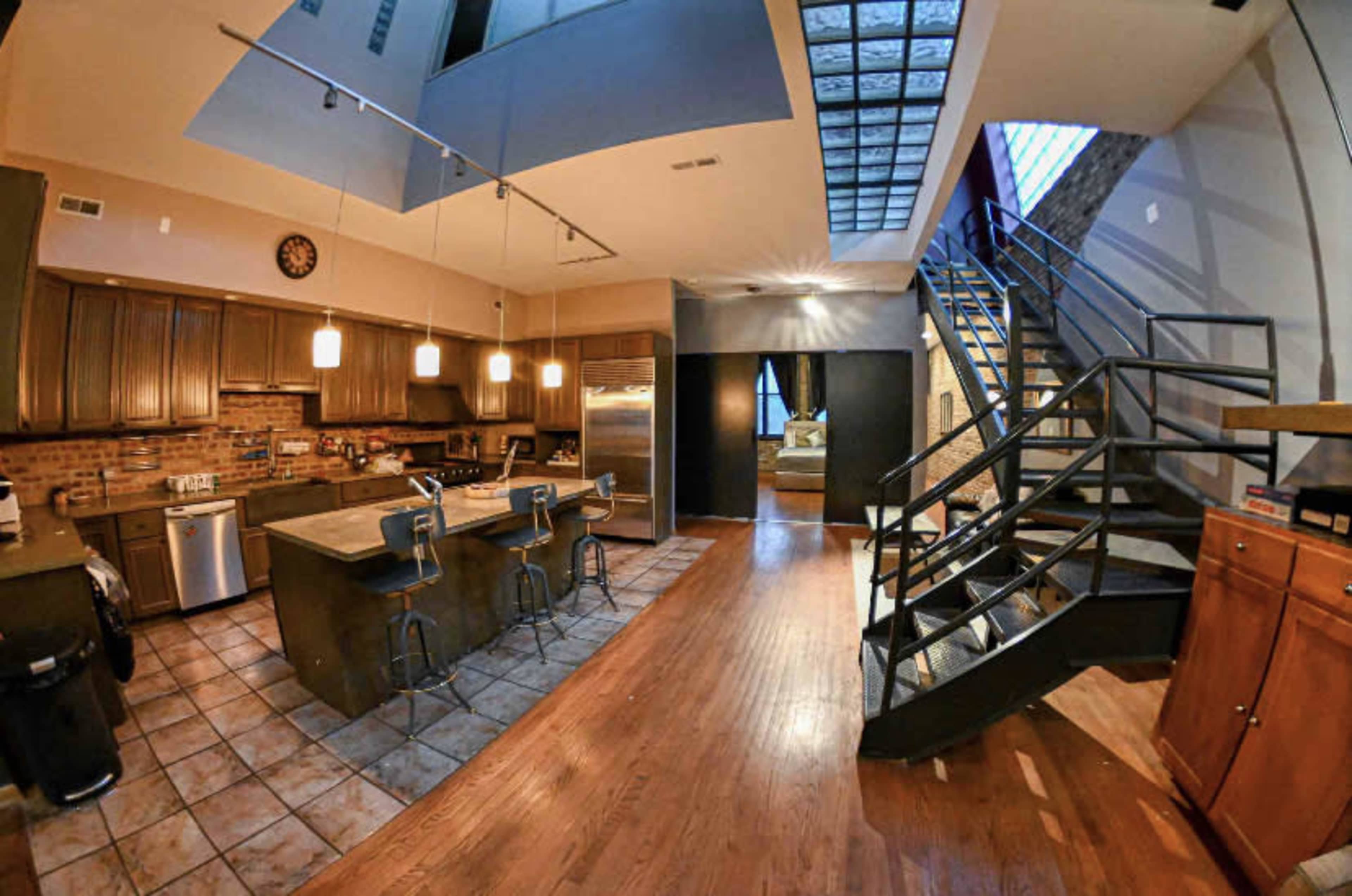 The image shows a spacious kitchen and dining area with wooden cabinets, stainless steel appliances, and a staircase leading to a second level.