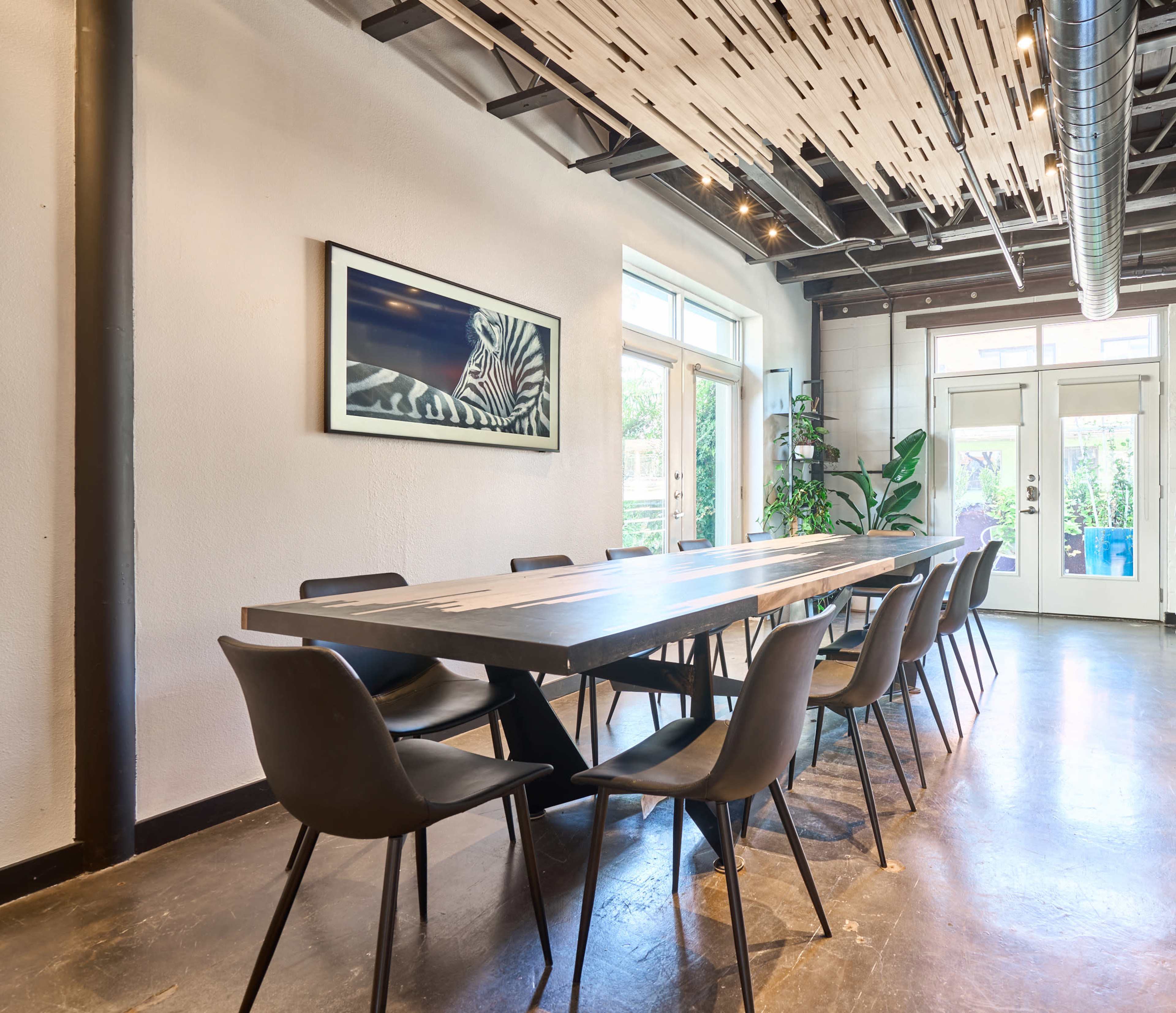 A spacious dining area features a long table surrounded by sleek black chairs, with large windows letting in natural light and a zebra print artwork on the wall.