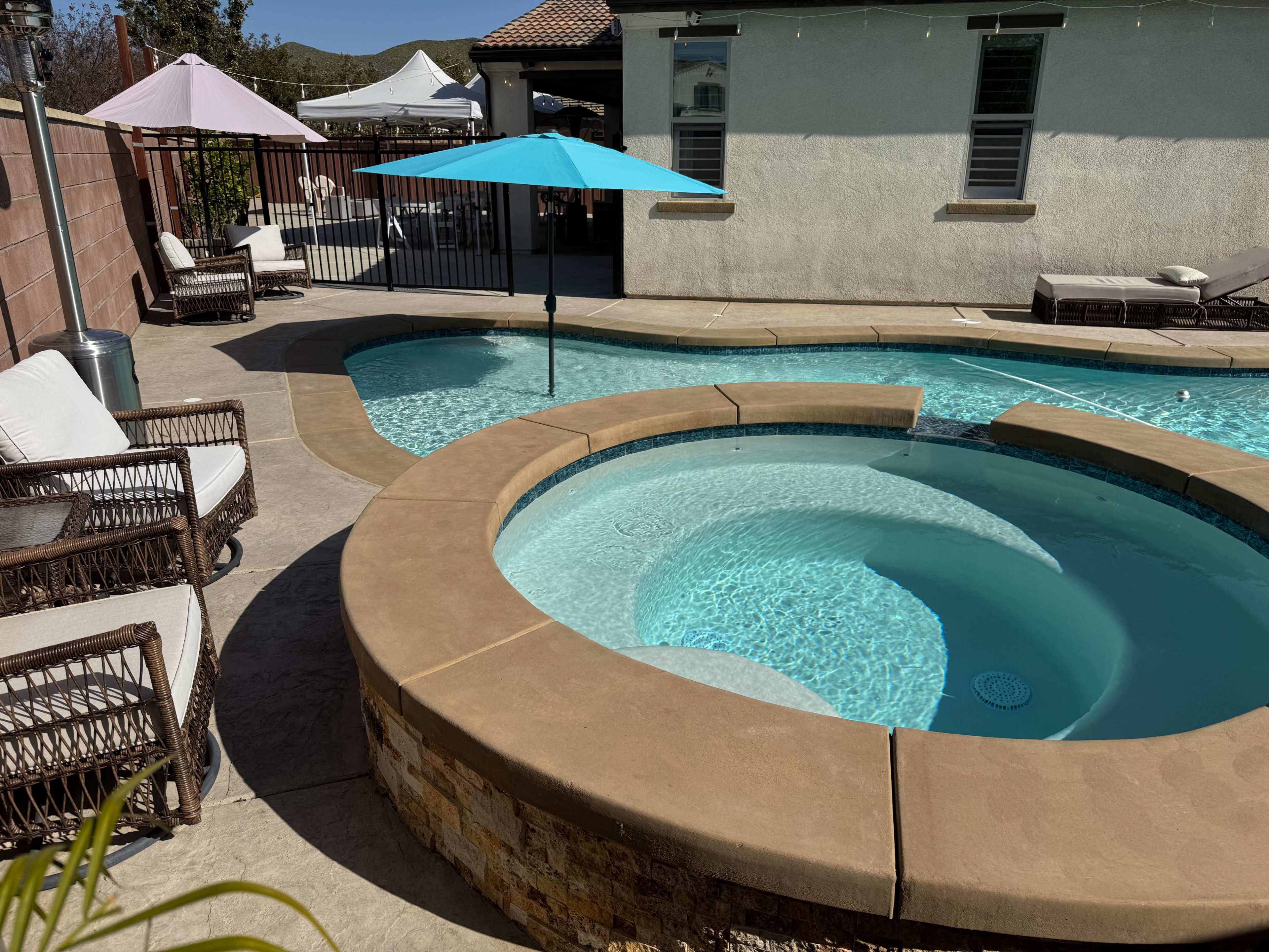 The image shows a backyard pool area featuring a circular hot tub with clear water, a turquoise umbrella, and several lounge chairs.