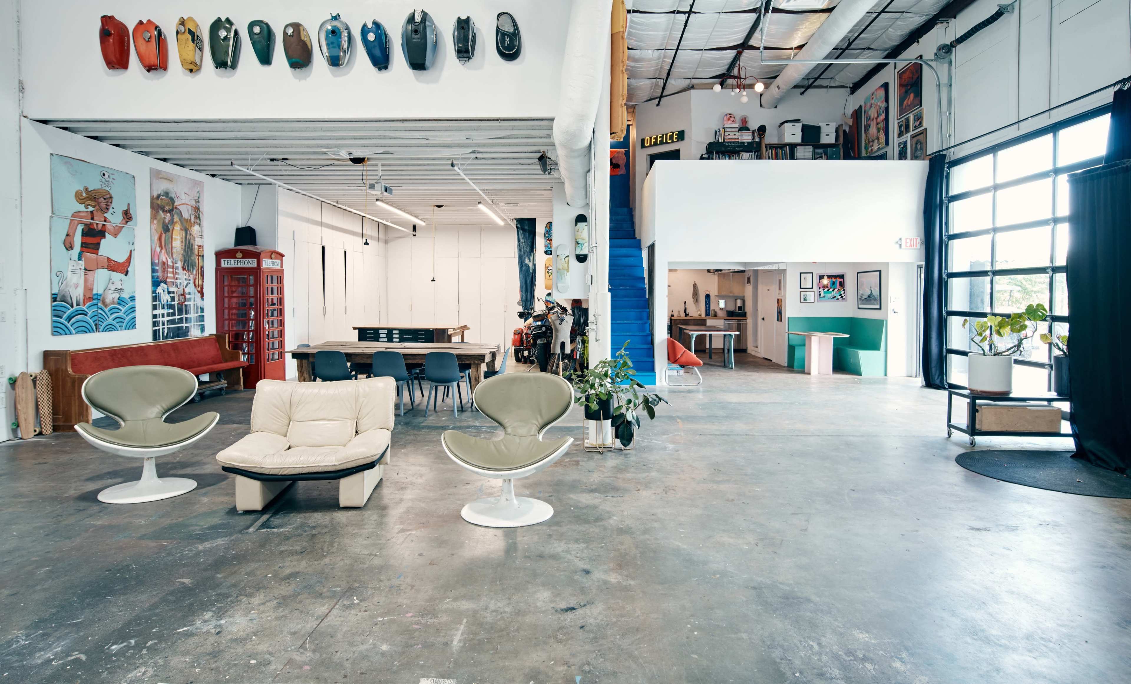 A spacious, modern interior with a mix of seating, artwork on the walls, and a large window illuminating the area.