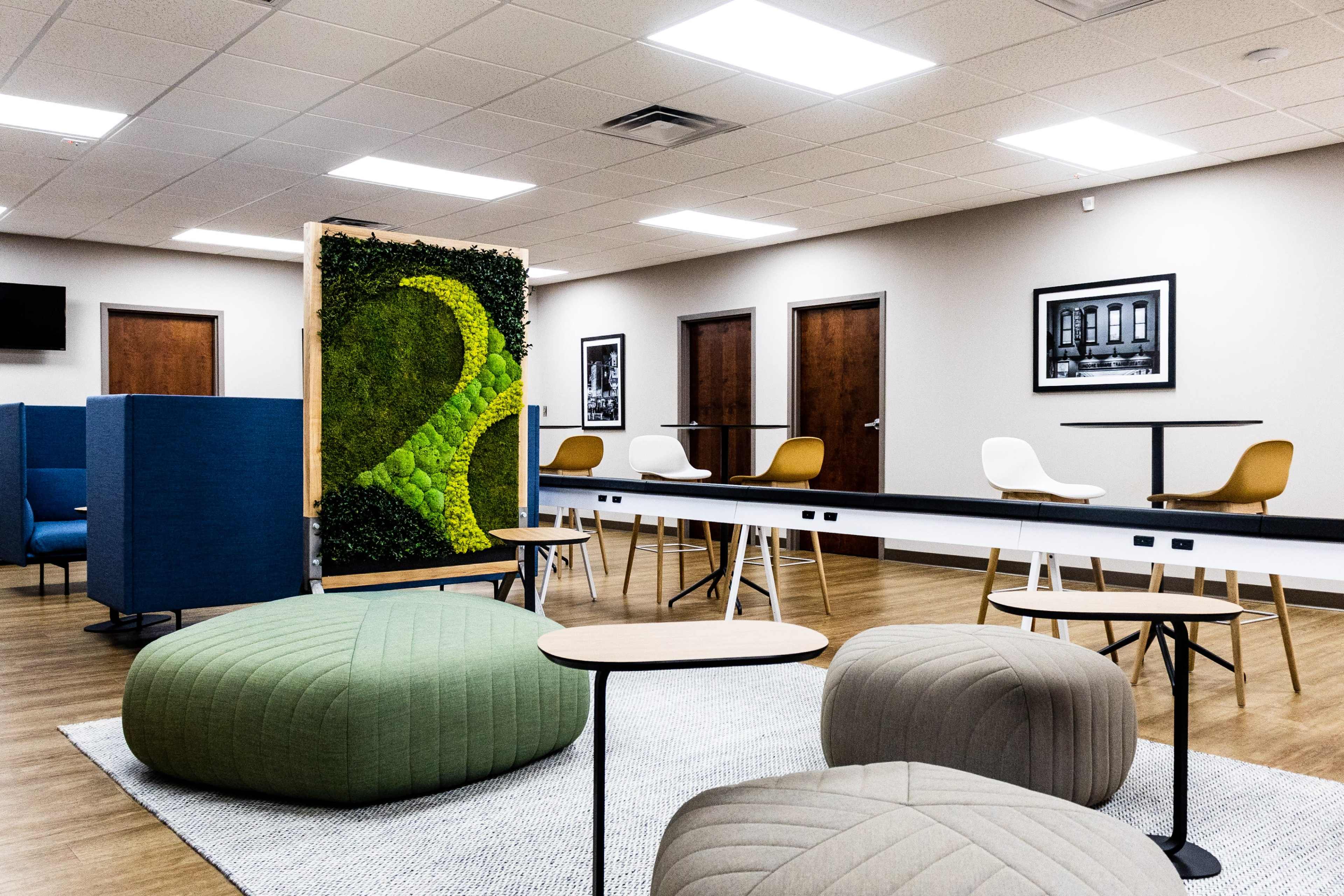 The image shows a modern interior office lounge area with seating arrangements, green decor, and tables.