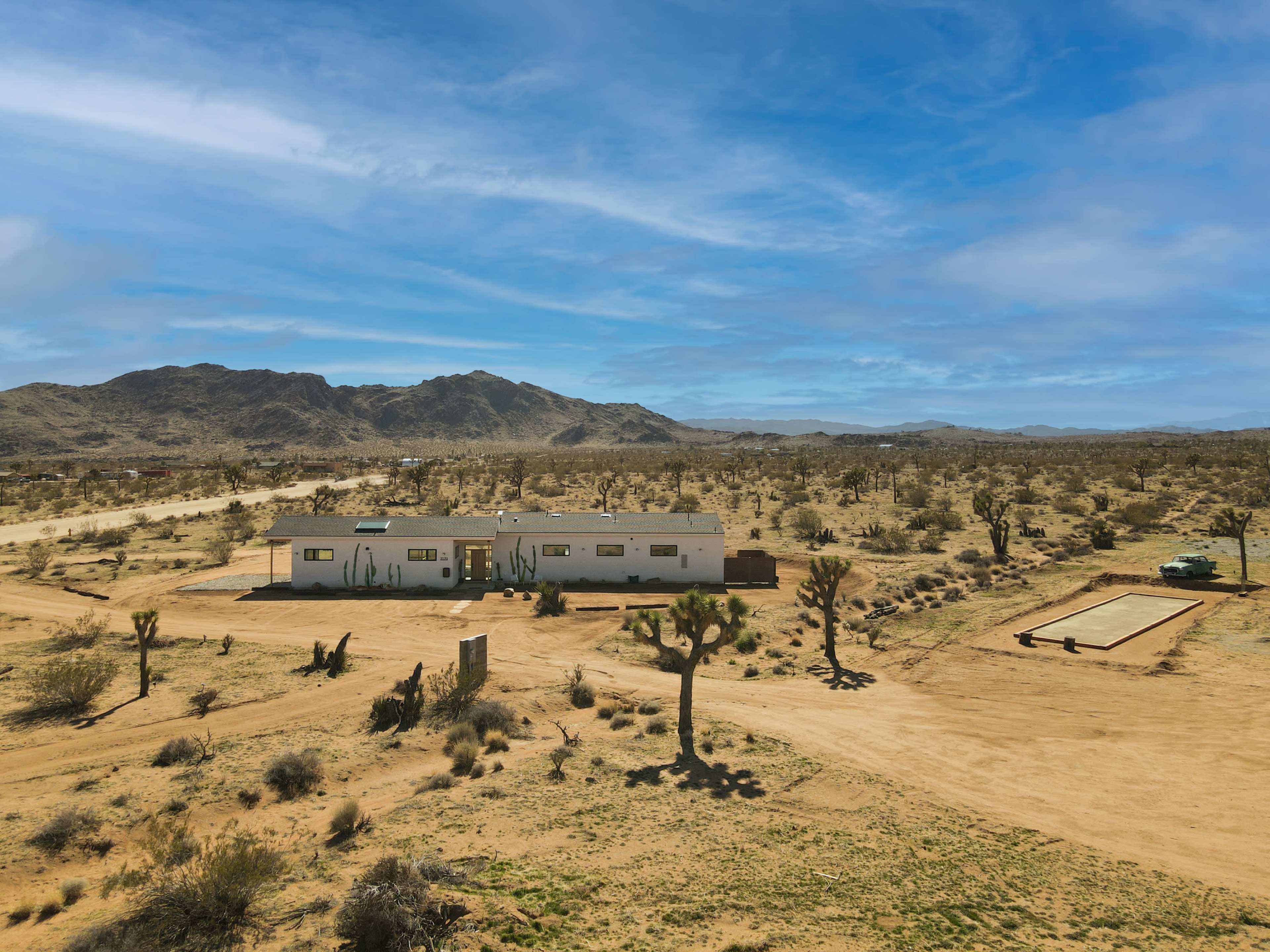 A white house stands in a desert landscape surrounded by sparse vegetation and mountains in the background.