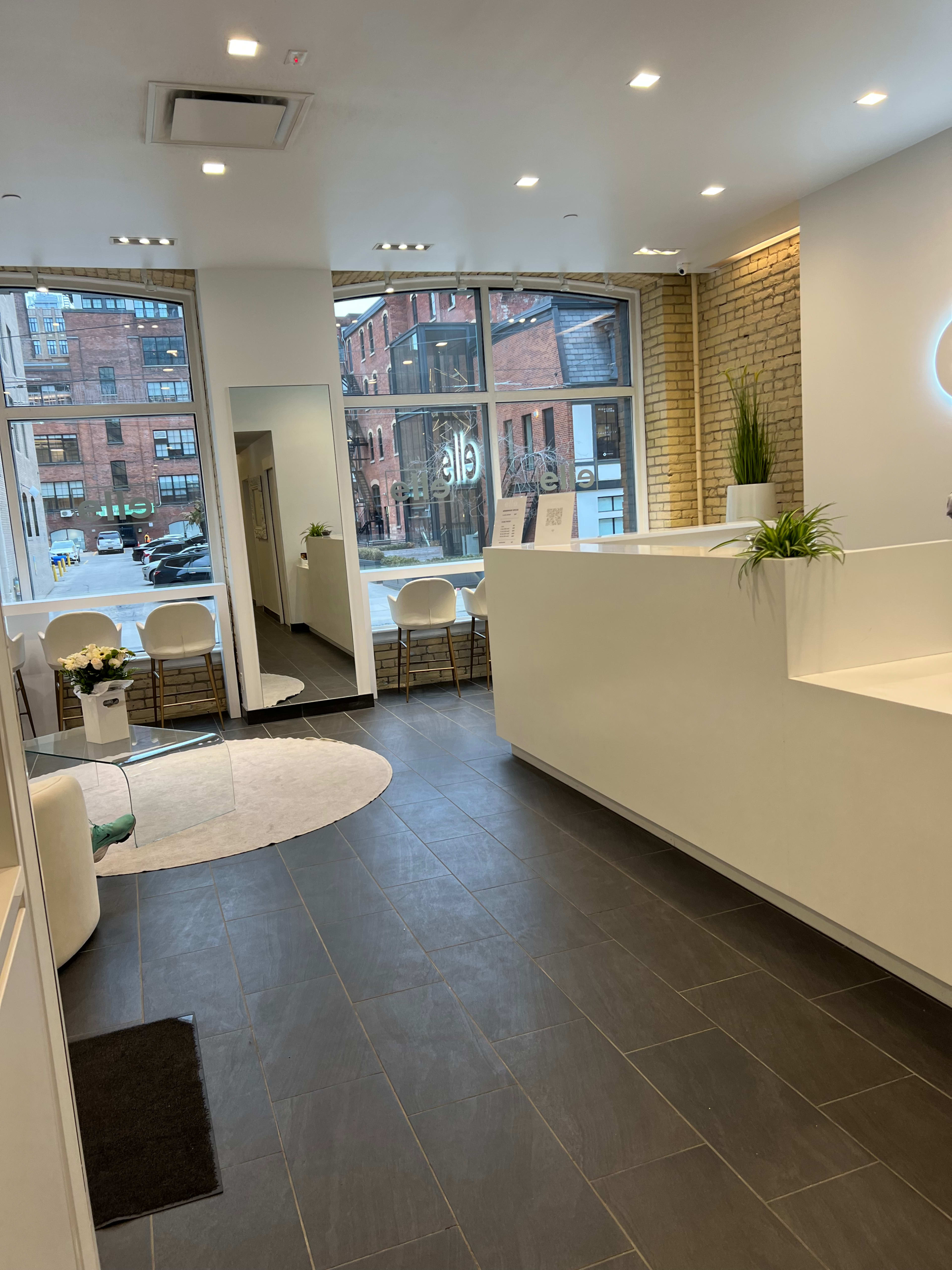 A modern, well-lit reception area of a spa or salon with white walls, dark tiled flooring, and a large mirror.