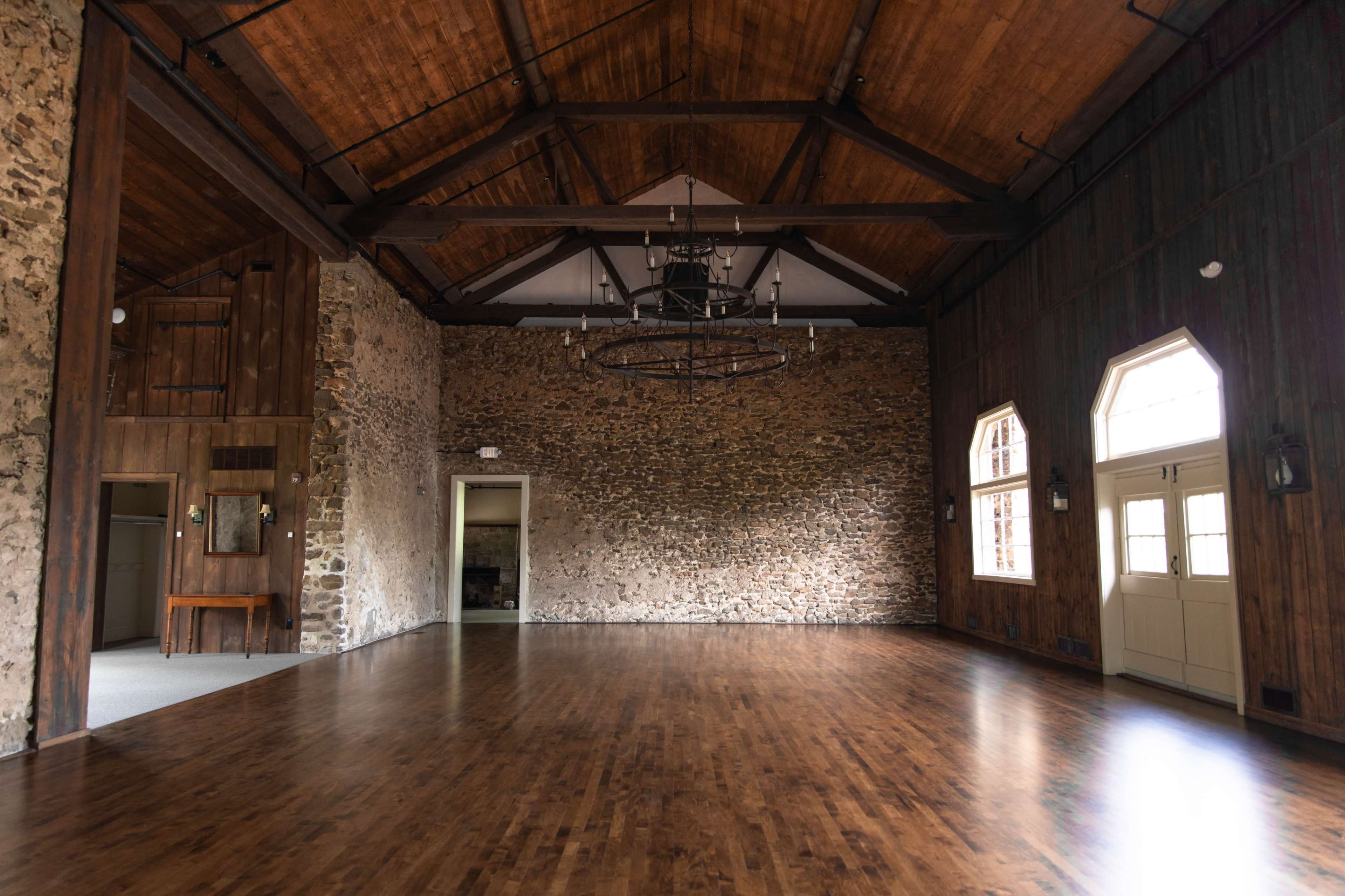 The spacious interior features exposed stone walls, wooden beams, and large windows, illuminated by a central chandelier.