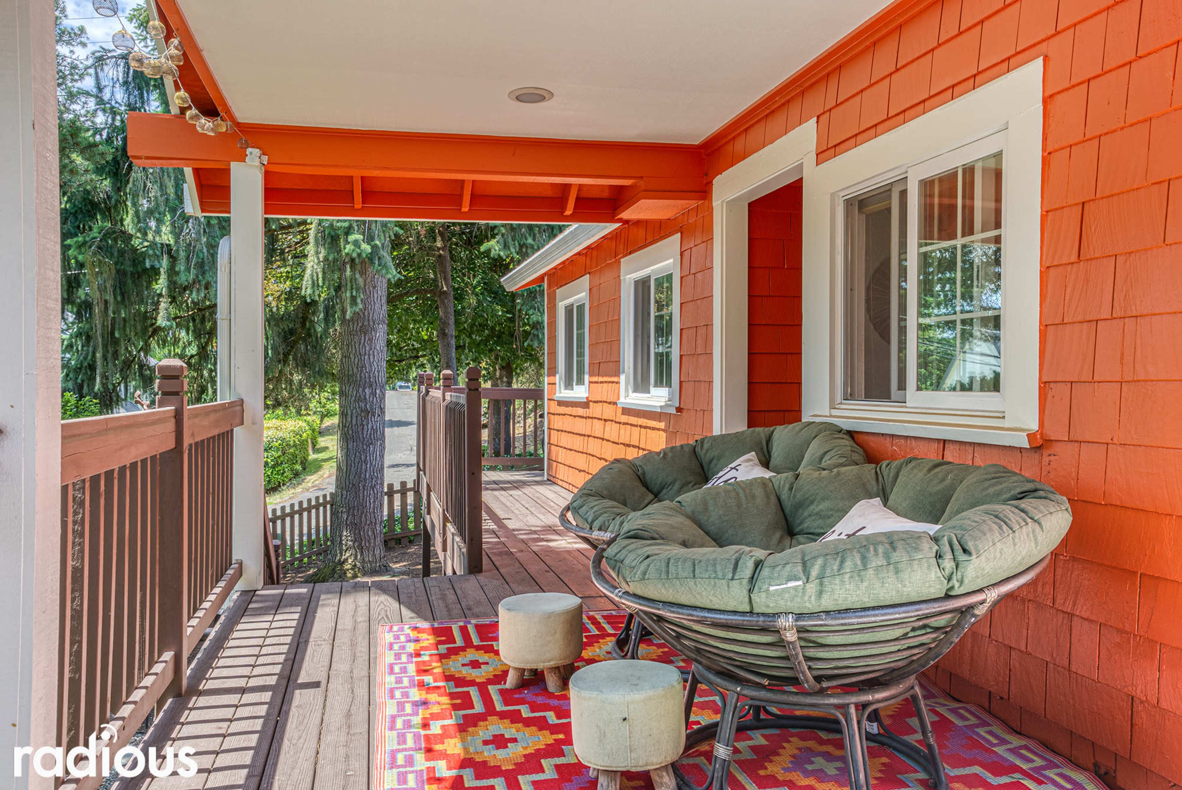 A porch with an oversized round chair, a colorful patterned rug, and an orange accent wall.