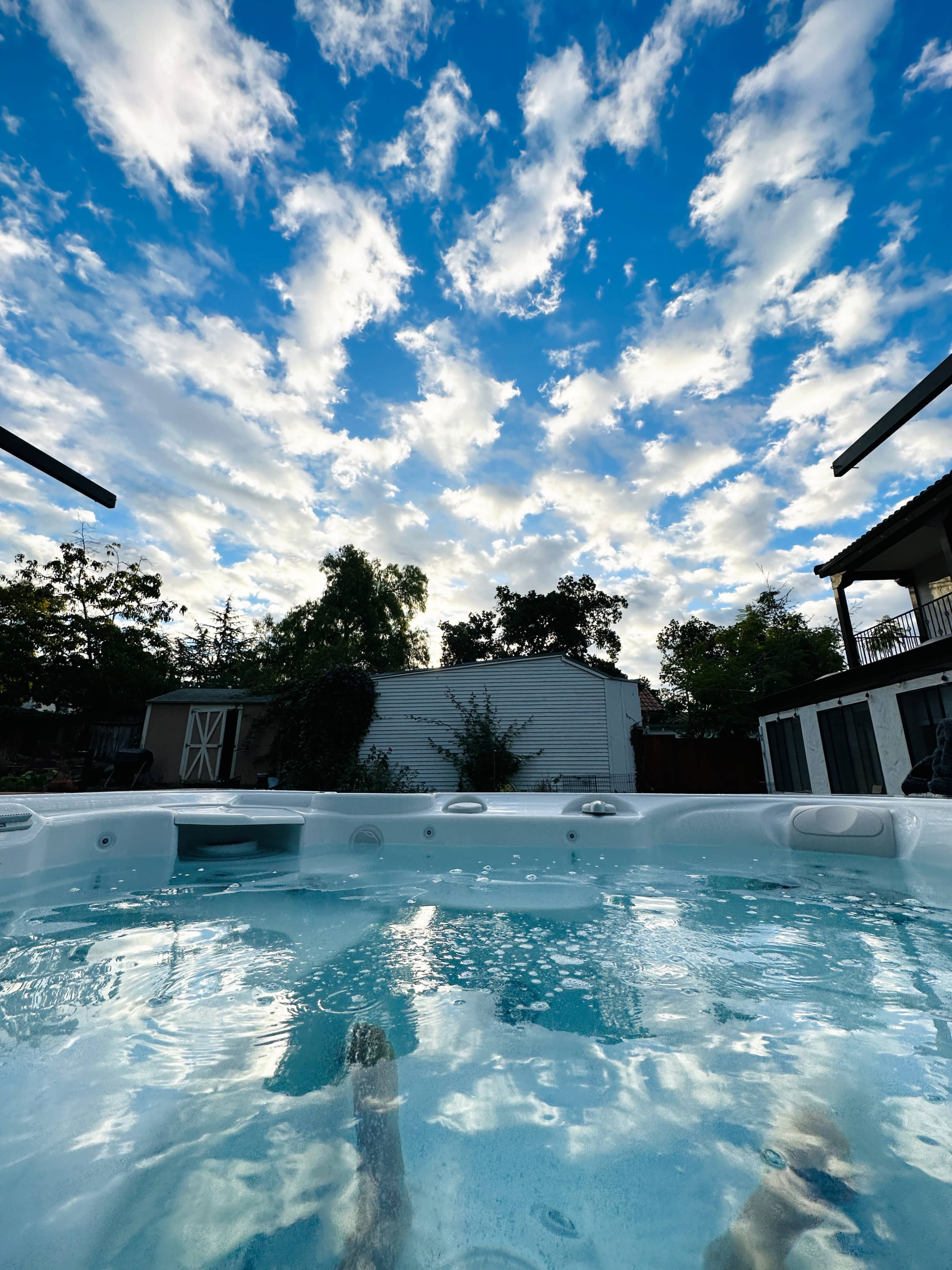 A hot tub filled with water reflects a sky filled with clouds on a clear day.