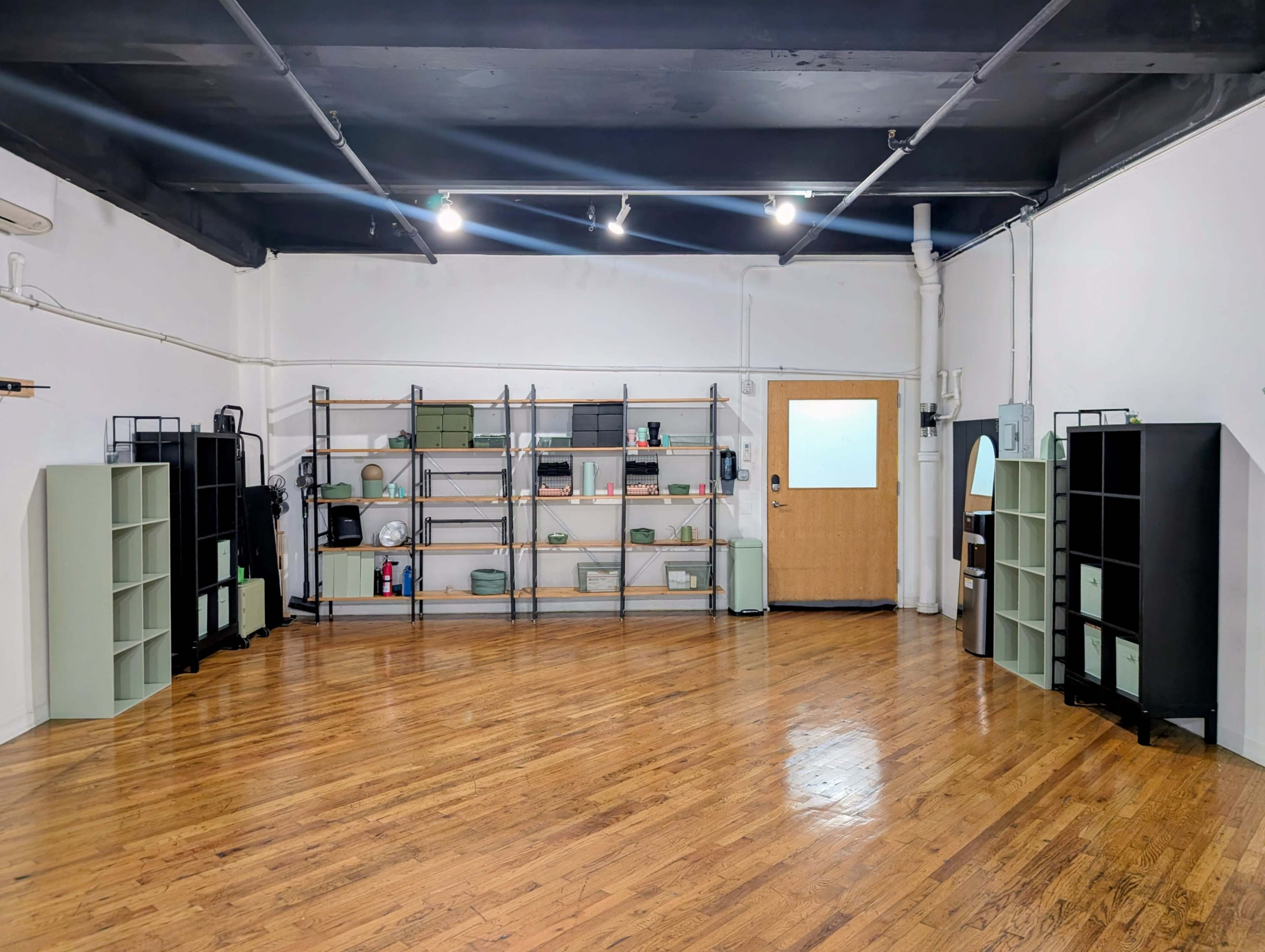 The image shows a spacious room with wooden floors and minimalist shelving units lining the walls.