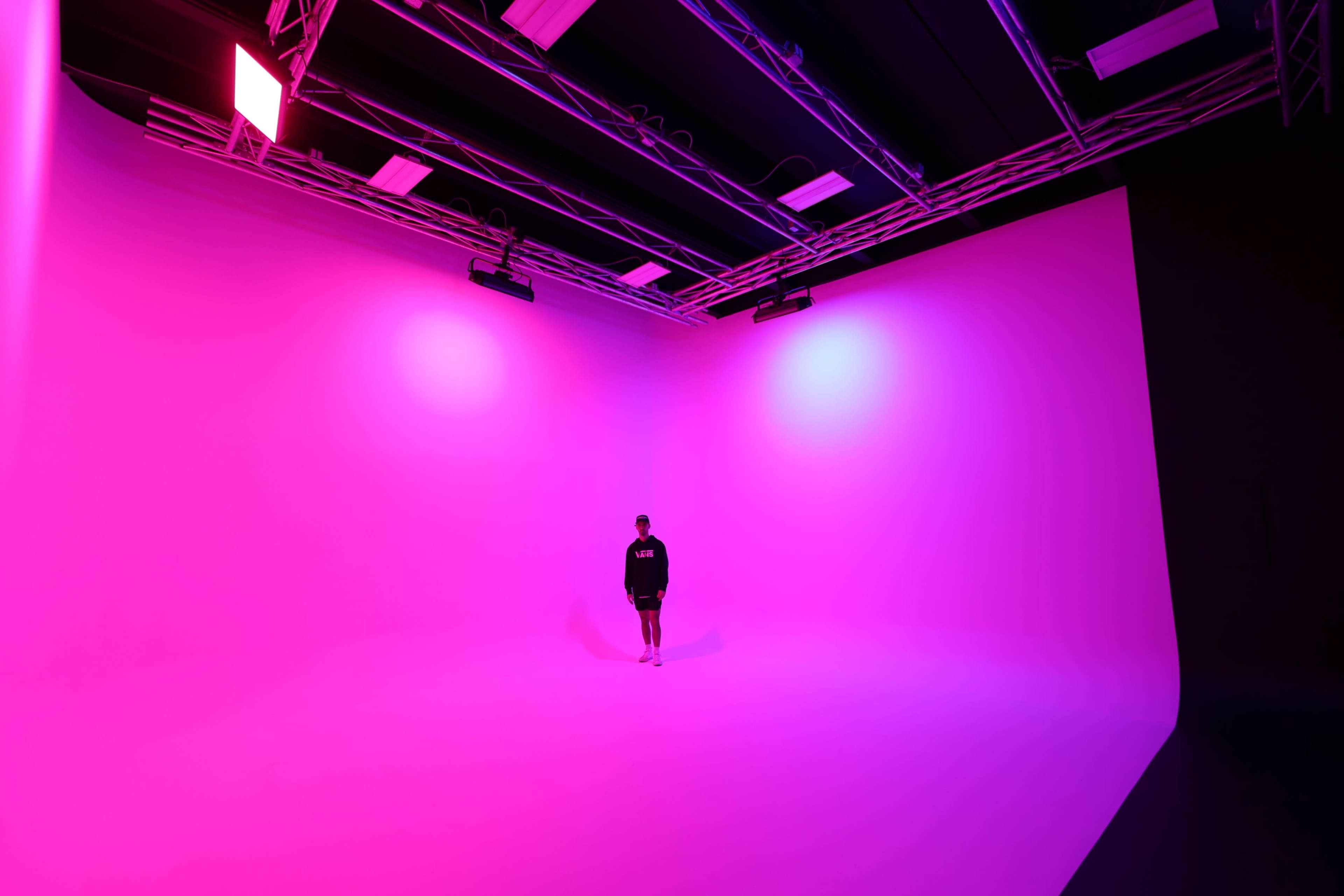 A person stands in a brightly colored studio space with pink lighting and seamless walls.