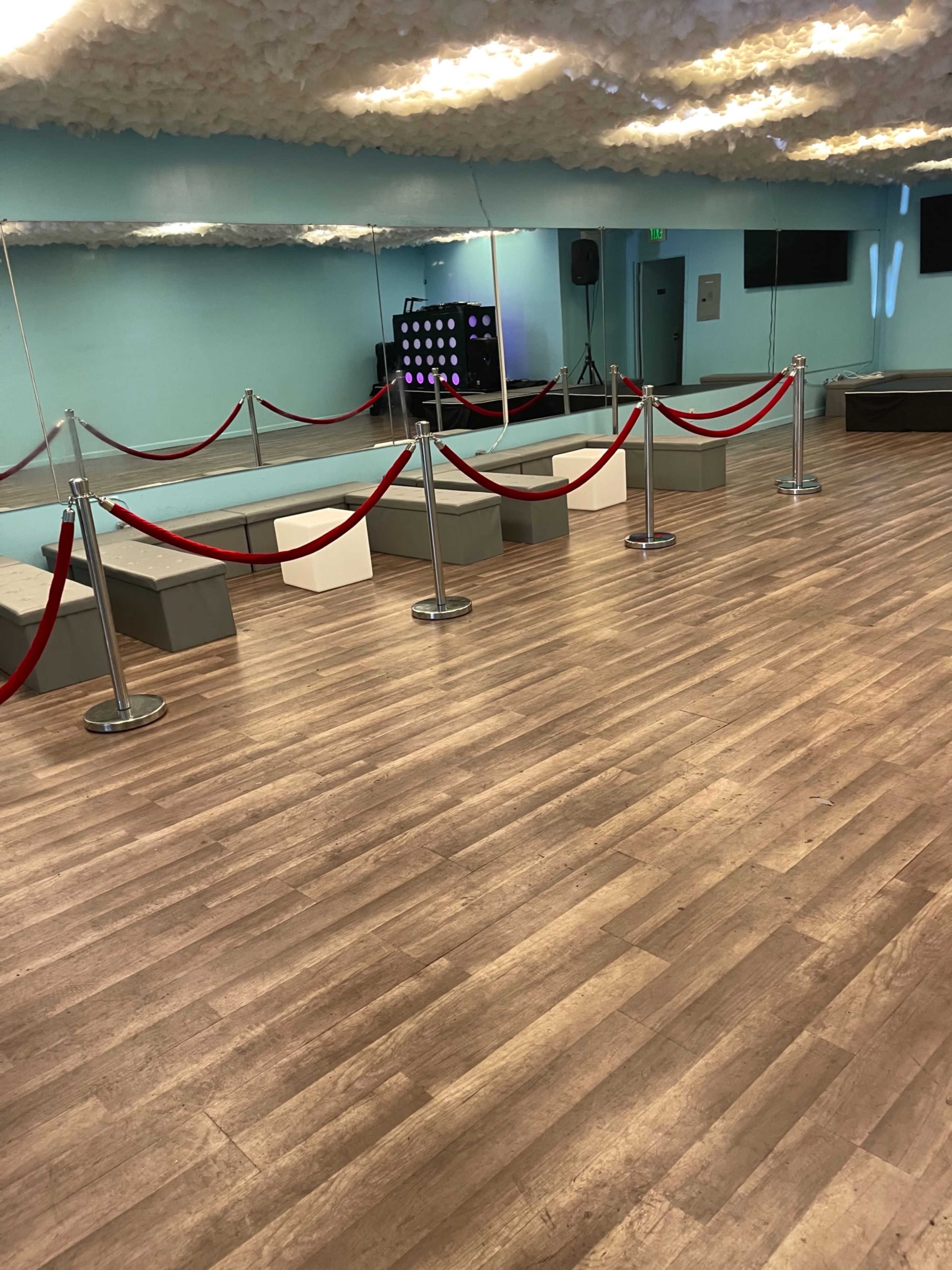 An empty dance studio with wooden flooring, mirrors on the wall, and a velvet rope barrier separating seating areas.