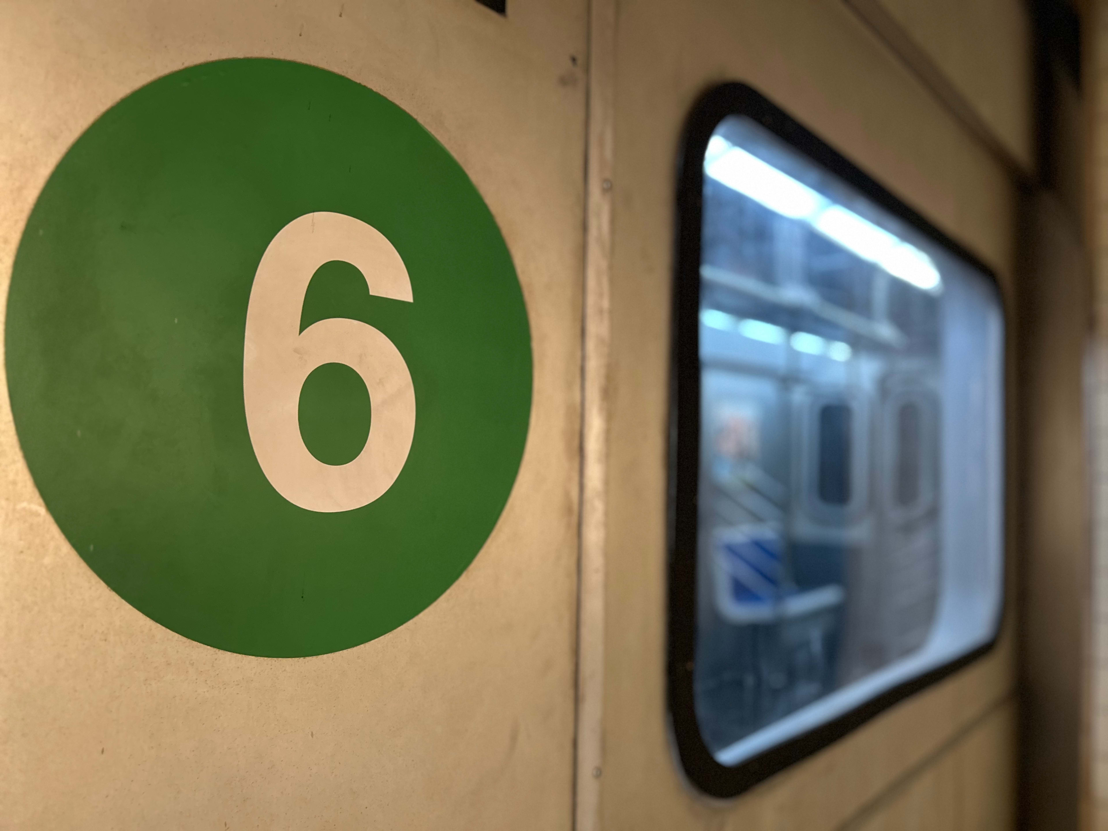 A green circular sign with the number 6 is mounted on a wall next to a train window.