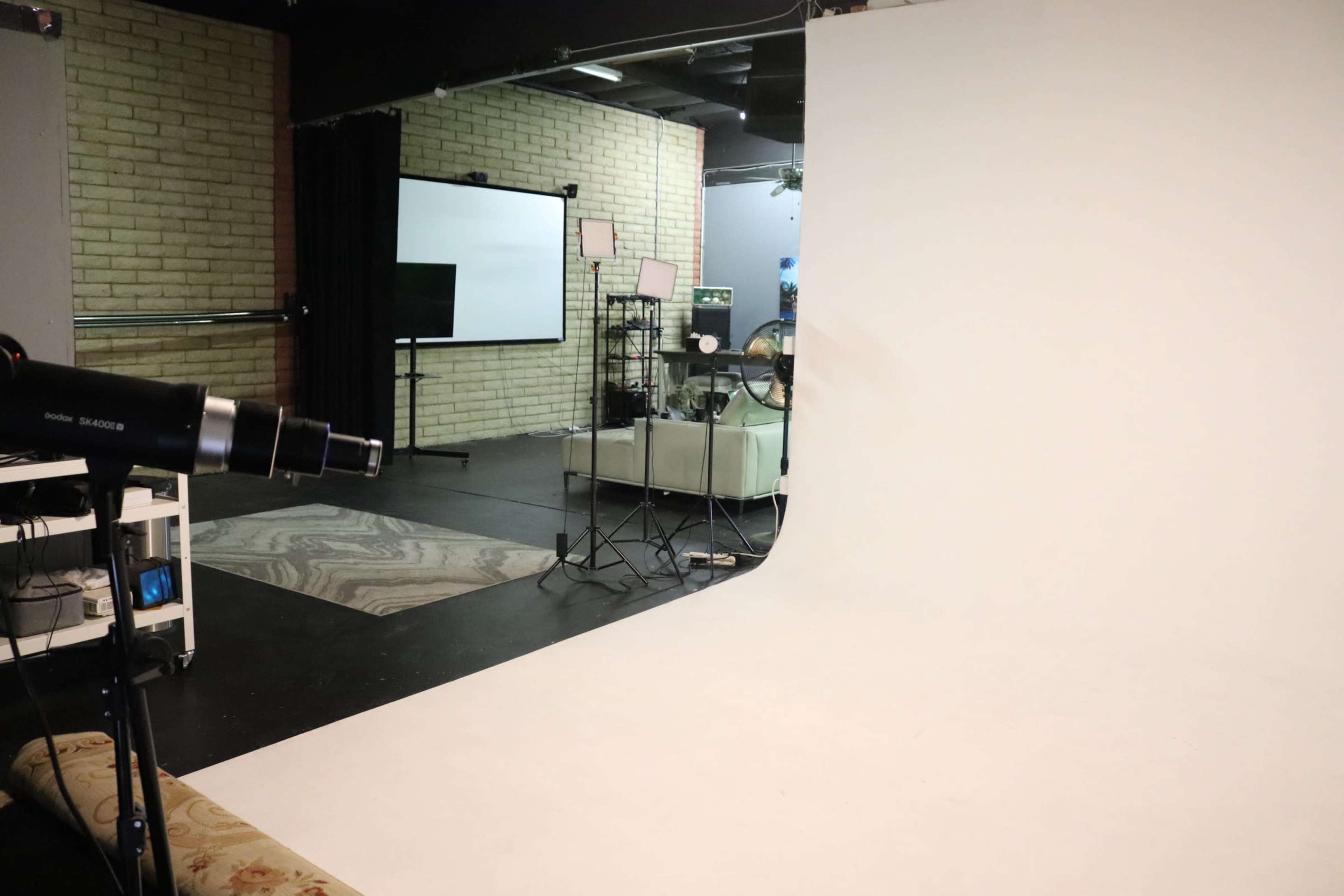 A photography studio features a seamless white backdrop, lighting equipment, and a minimalist setup with a couch and reflective surfaces.