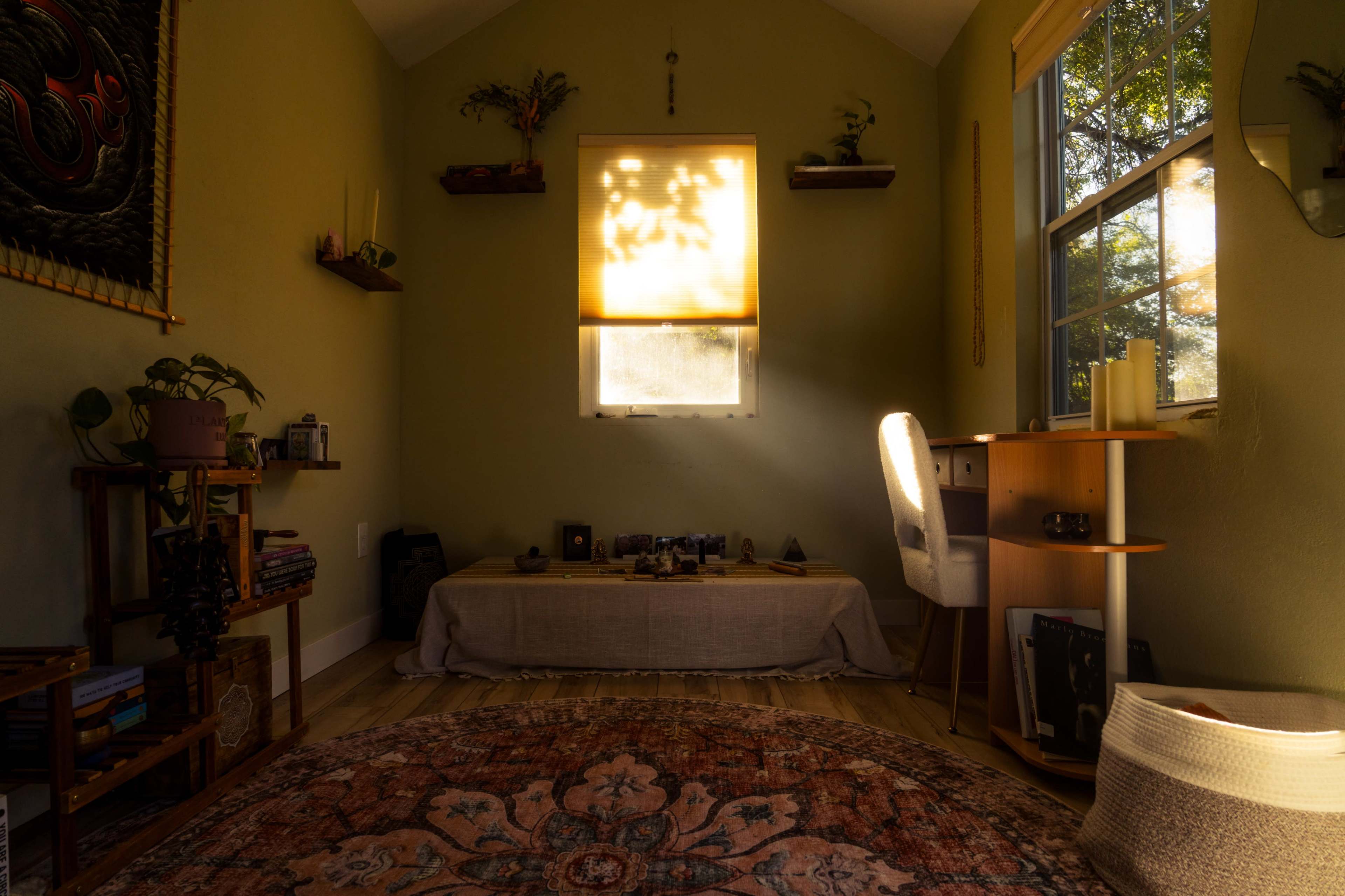 The image shows a serene interior space with green walls, a window filtered by a soft light, a wooden desk, a rug, and a small display of plants and decorative items.