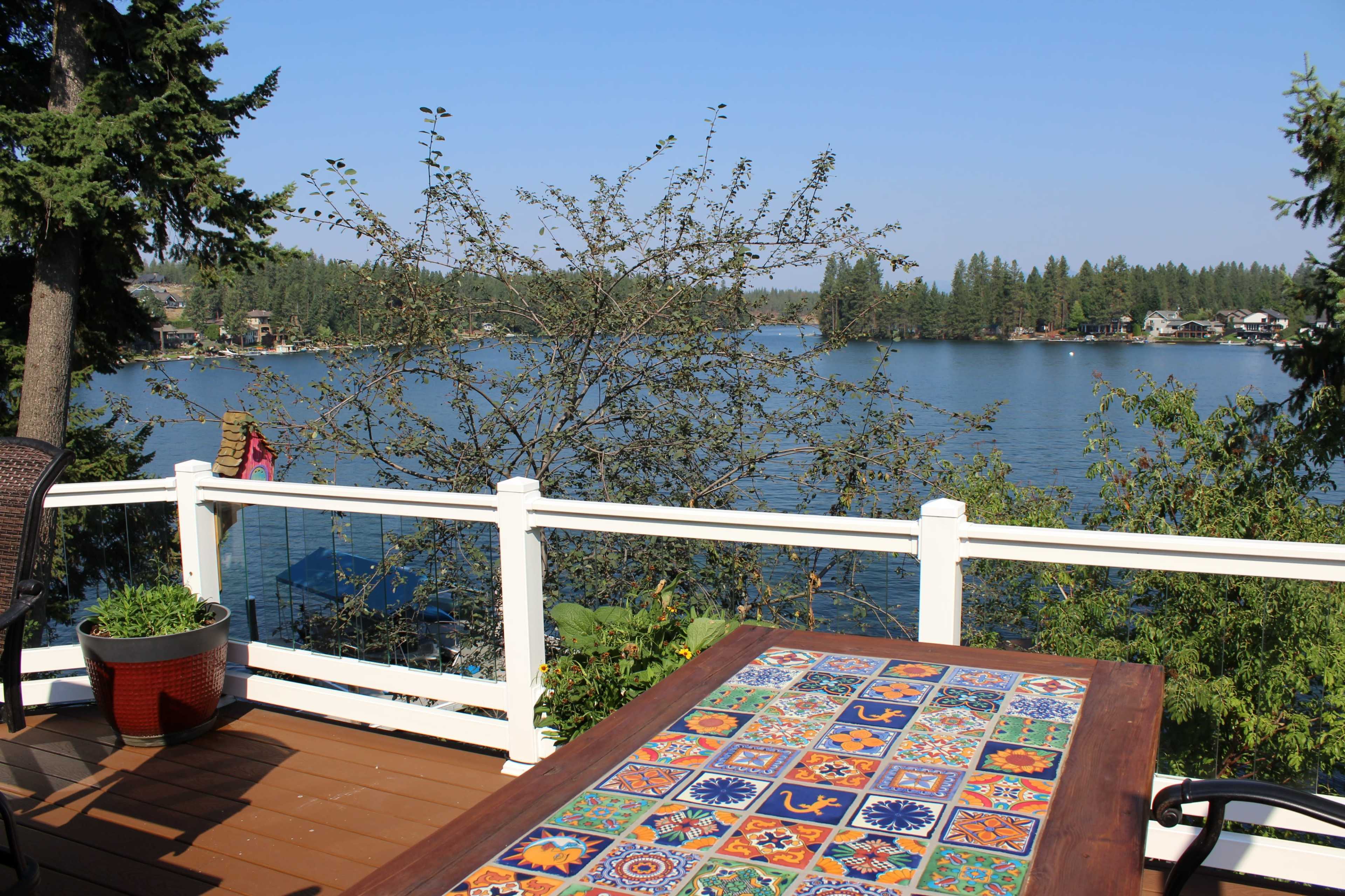 A patio table with colorful tiles overlooks a calm lake surrounded by trees.