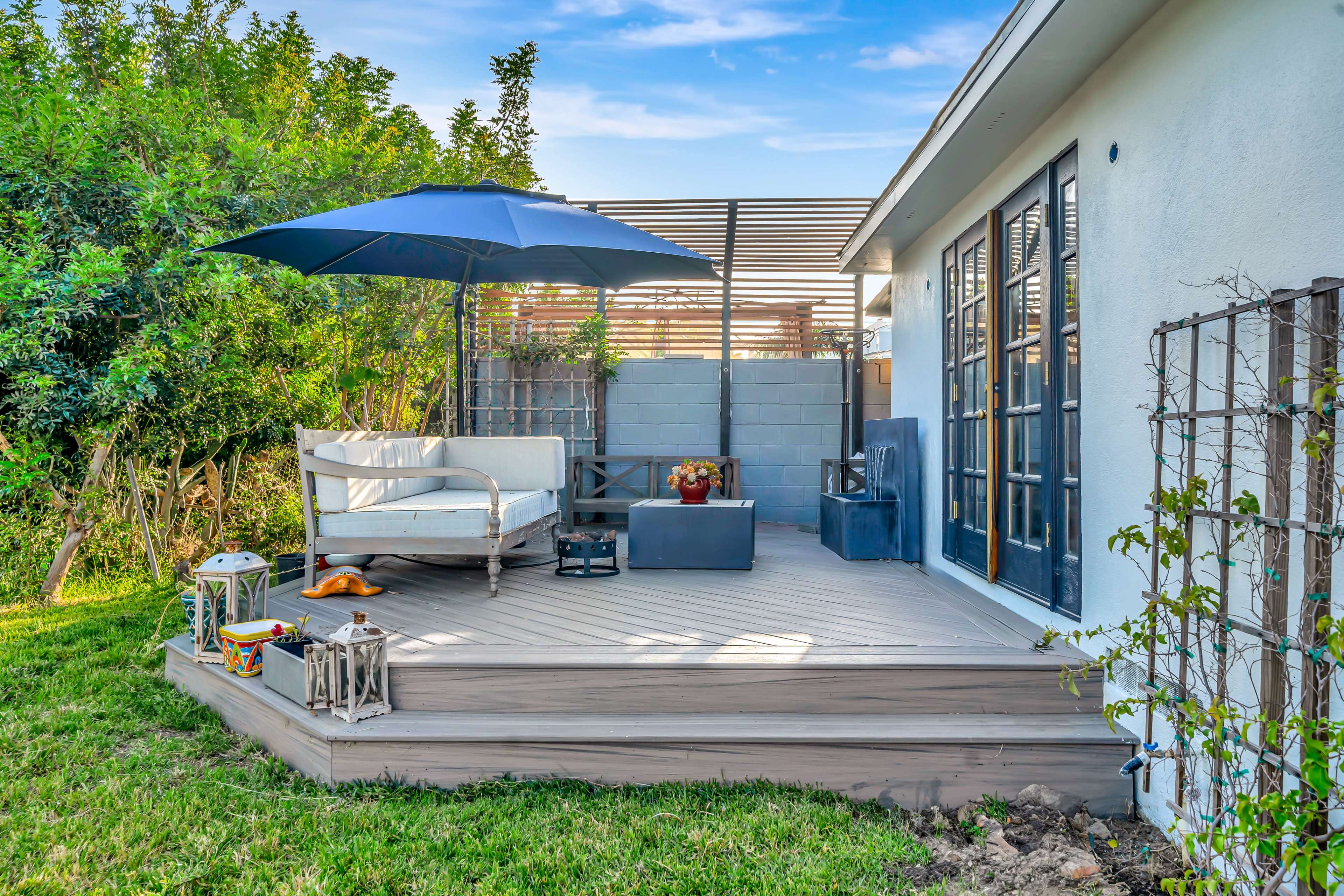 A wooden deck features an outdoor seating area with a large umbrella and surrounding greenery.