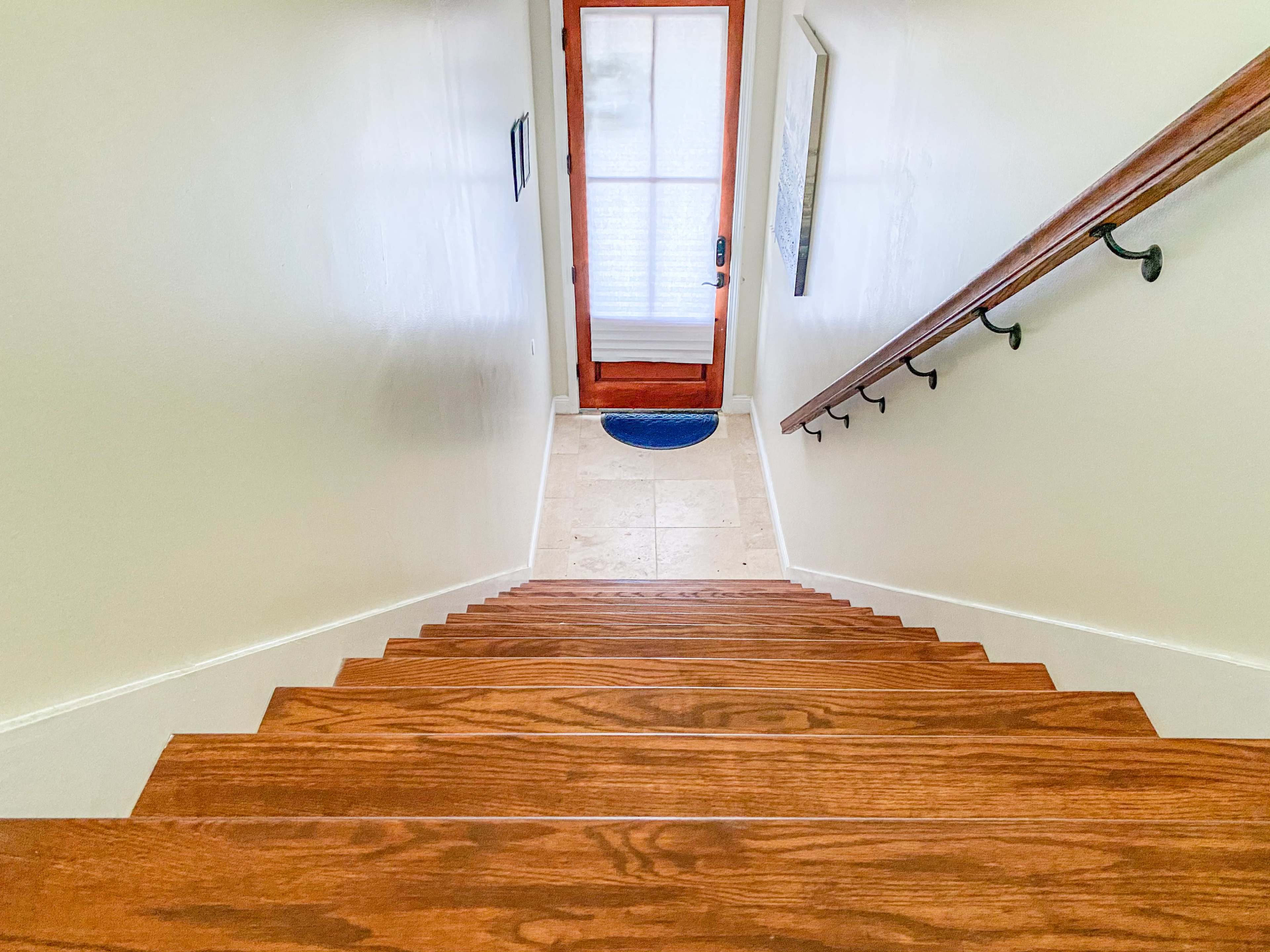 The image shows a wooden staircase leading down to a tile floor near a glass door.