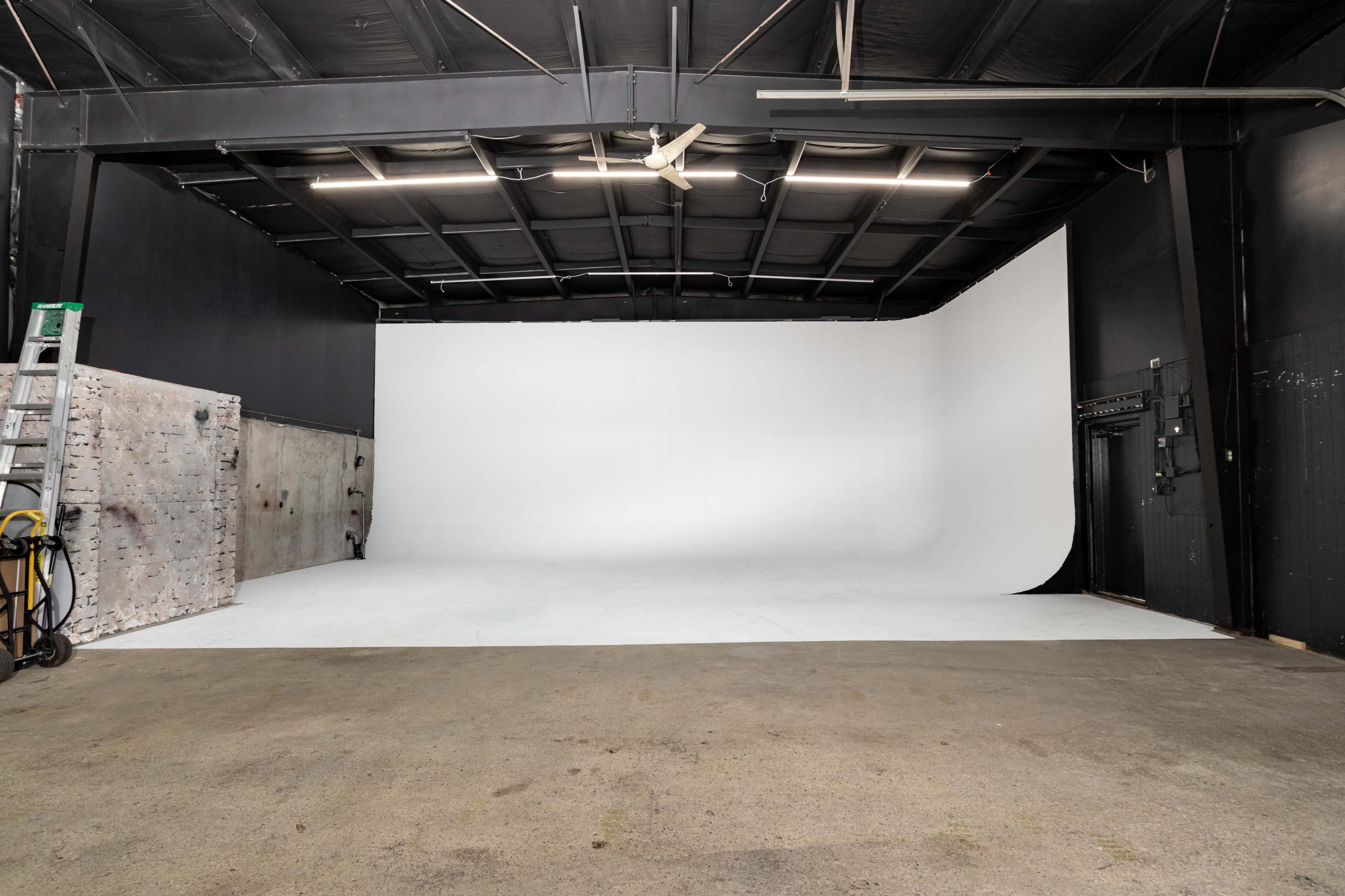 An empty photo studio with a white backdrop and a concrete floor.