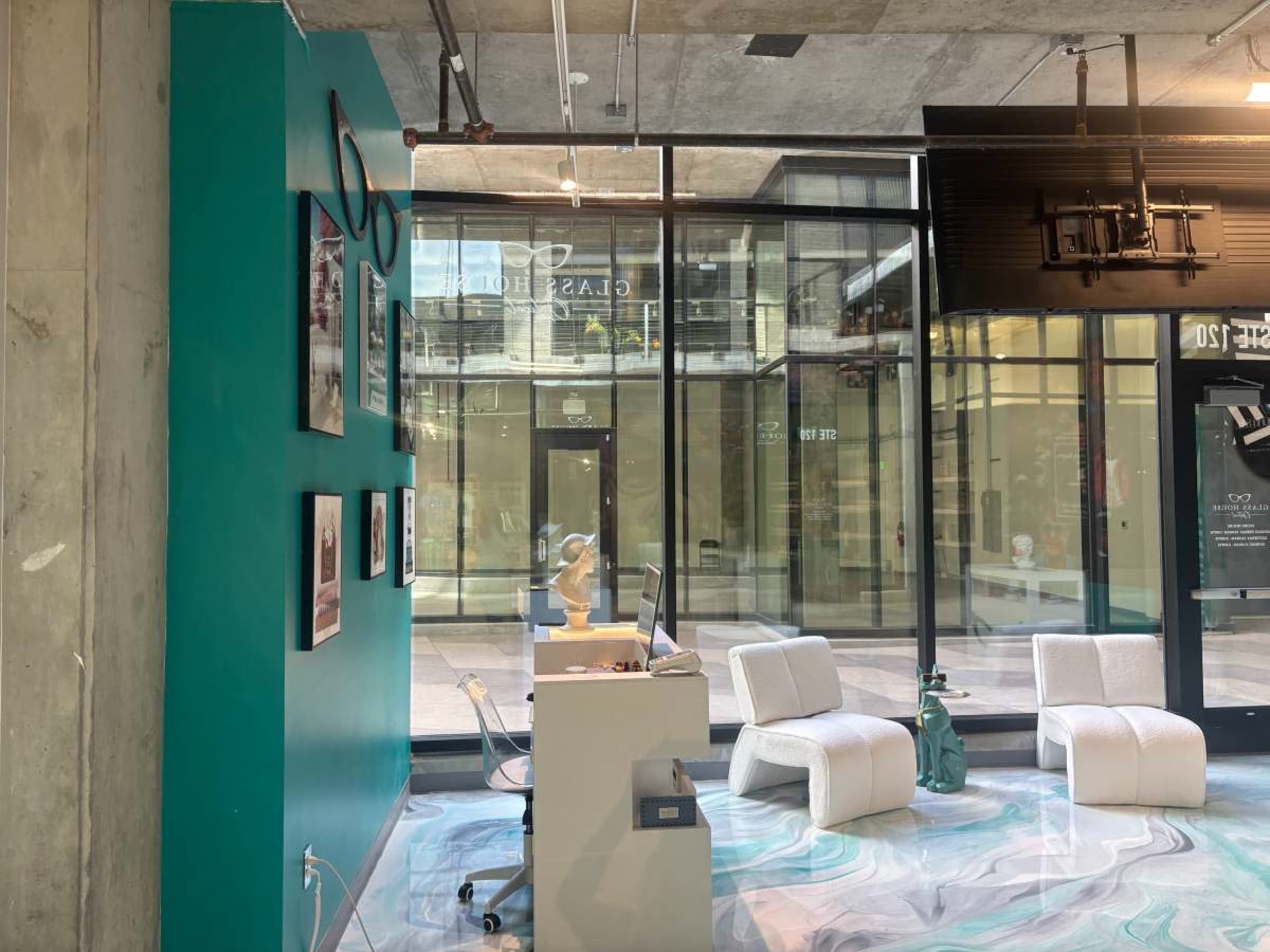 The image shows a modern interior of a store with teal walls, large windows, and minimalist furniture.