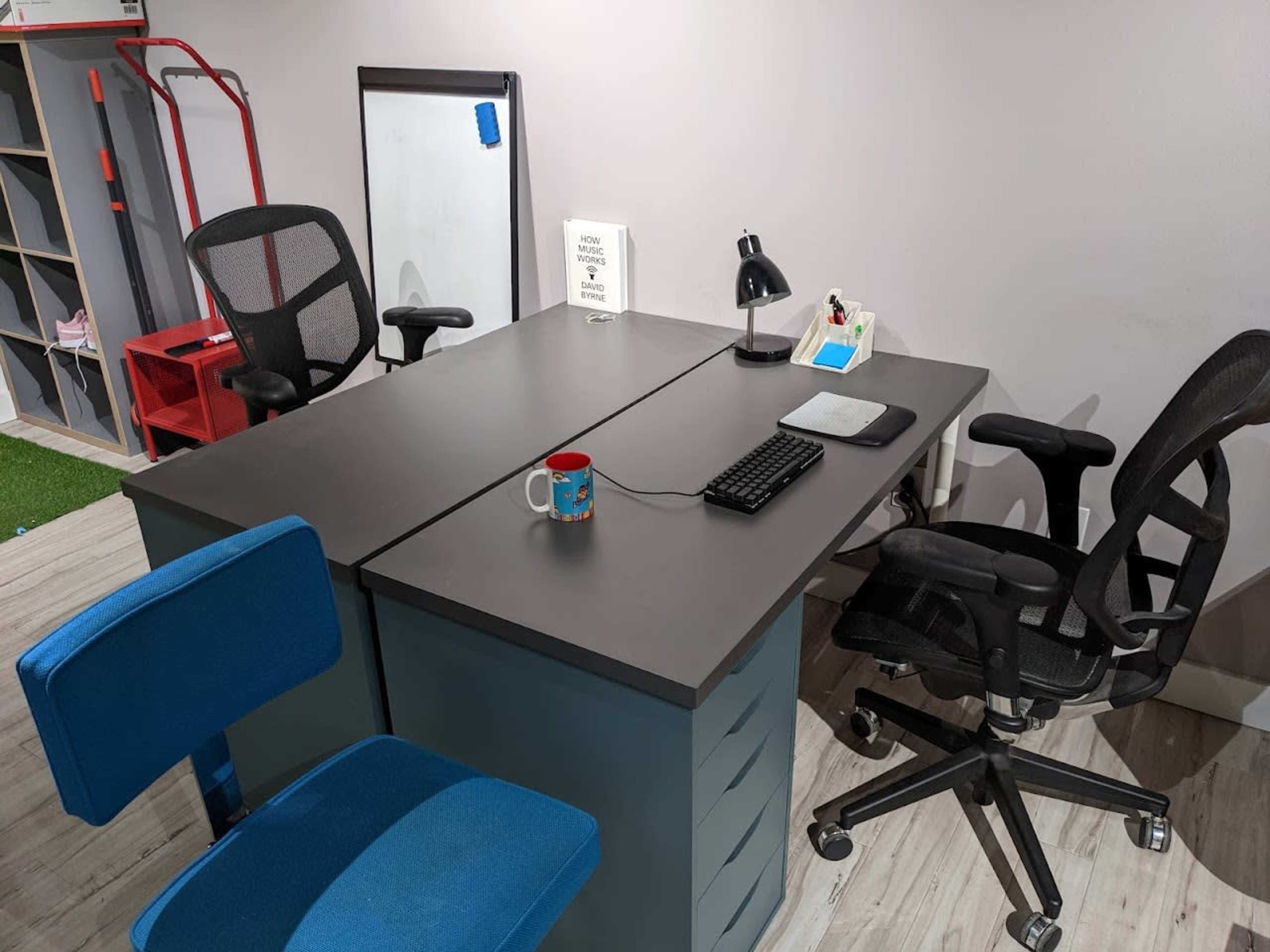 A modern office space with a double desk, two office chairs, a lamp, a keyboard, a laptop, and a mug on the table.