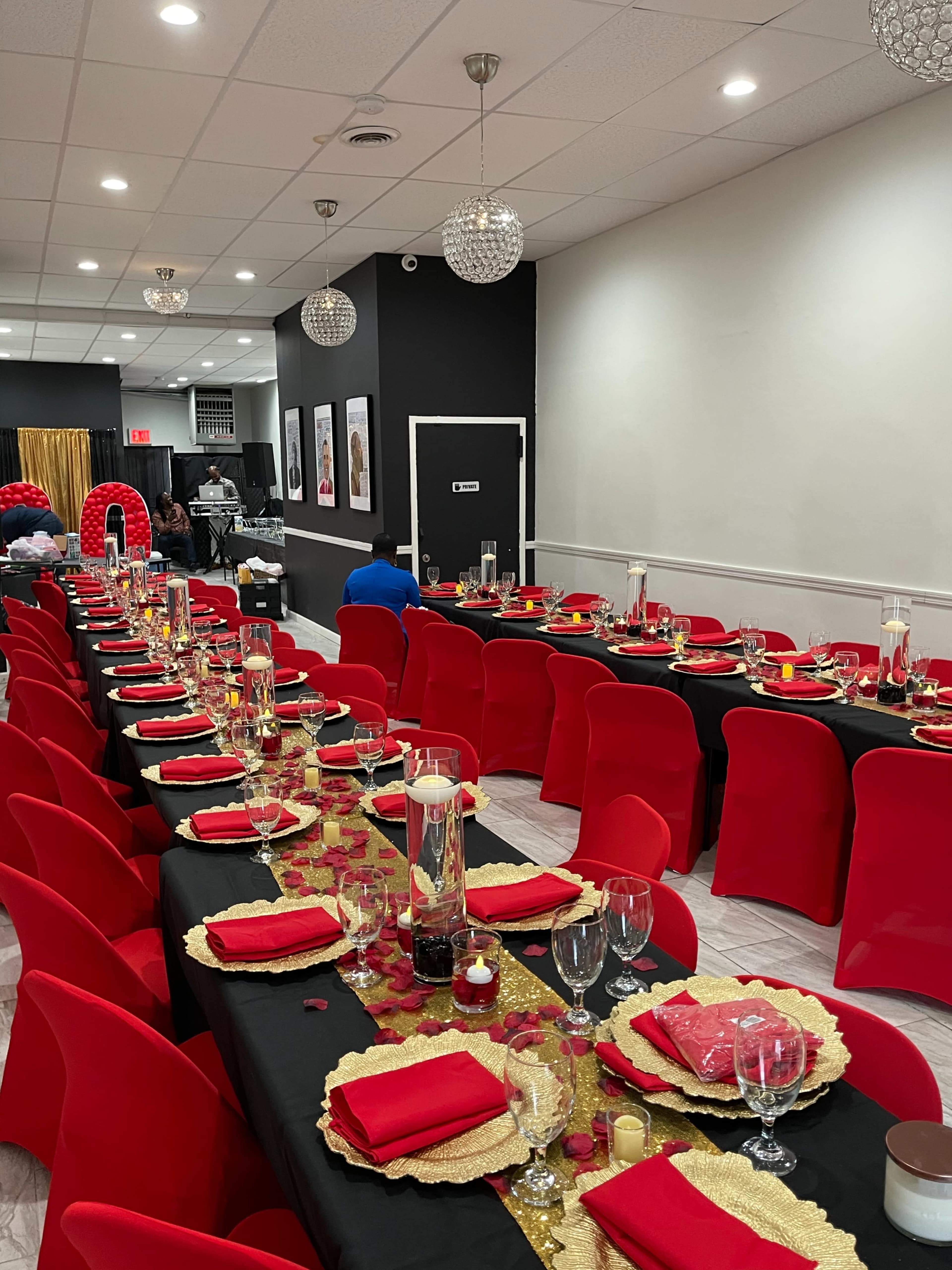 A festive dining setup with long tables covered in black cloth, red chairs, and decorative centerpieces featuring candles and gold accents.