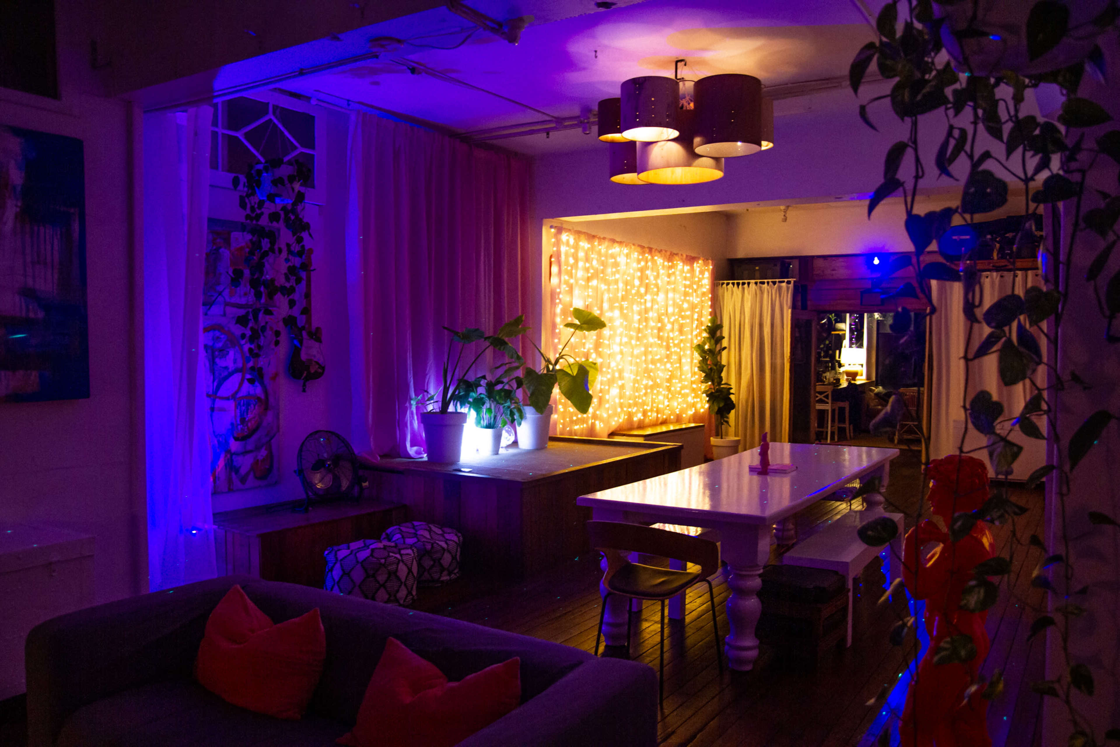 A cozy interior space featuring a large table, soft seating, and decorative lights along the walls.