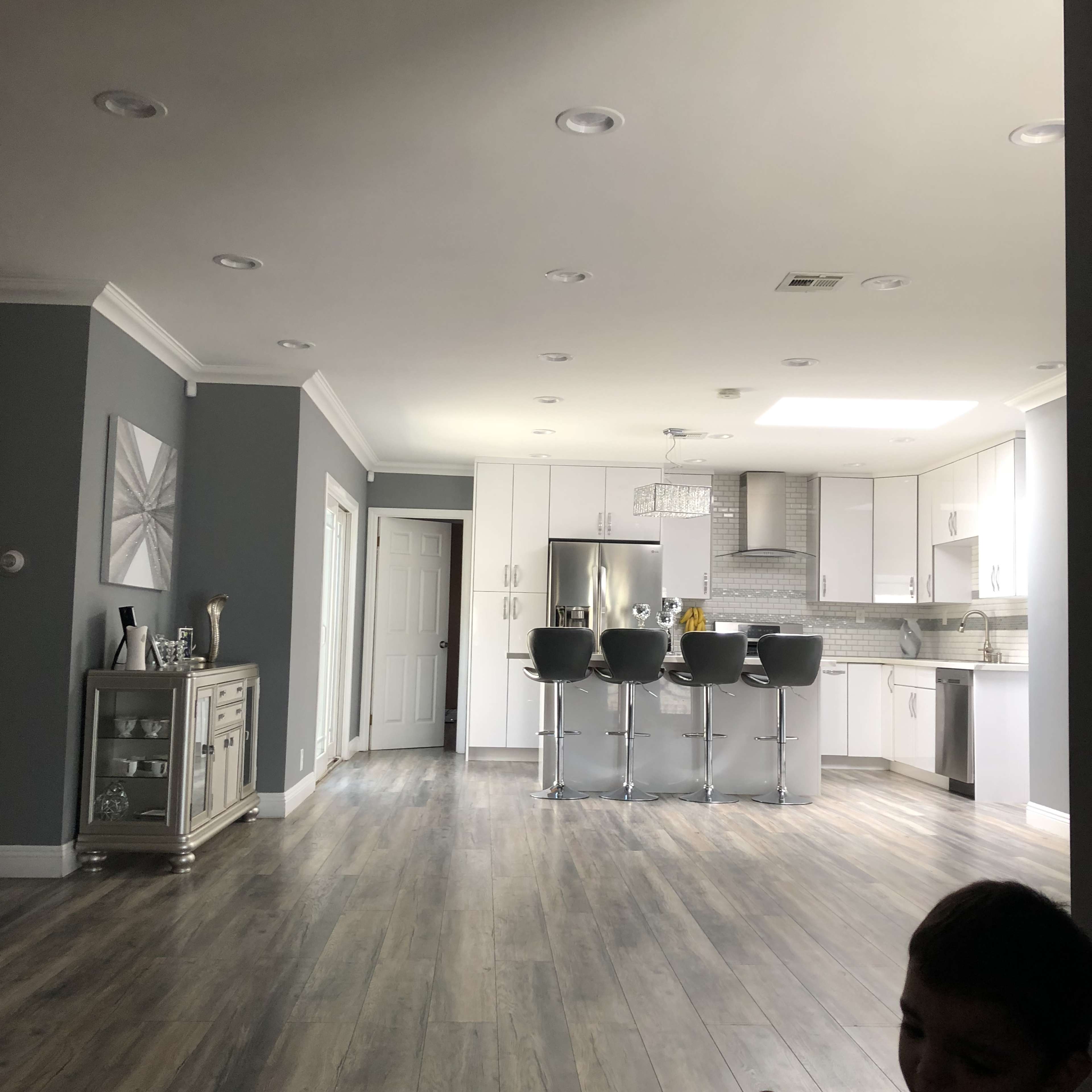 A modern kitchen features white cabinetry, a central island with bar stools, and gray walls, with wooden flooring throughout.